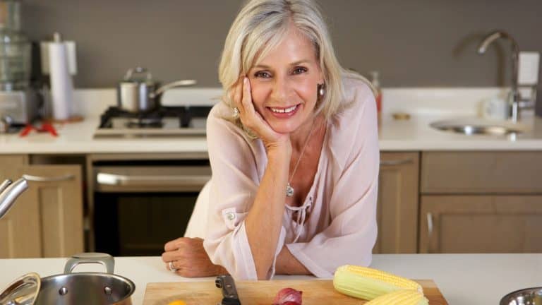Close up portrait of older beautiful woman leaning on kitchen counter with fresh produce
