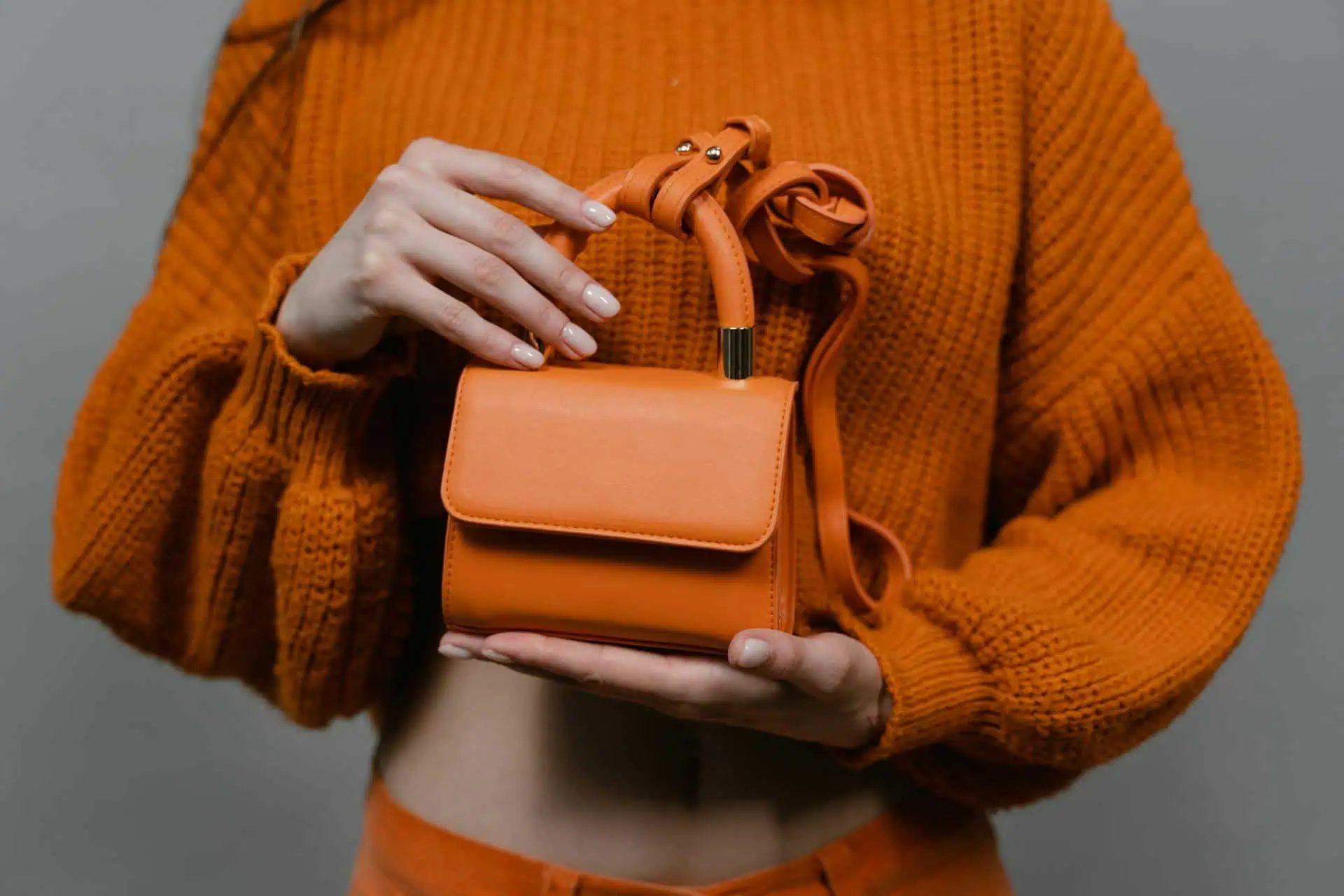 Mini Orange Leather Bag held by a Person wearing Knitted Sweater