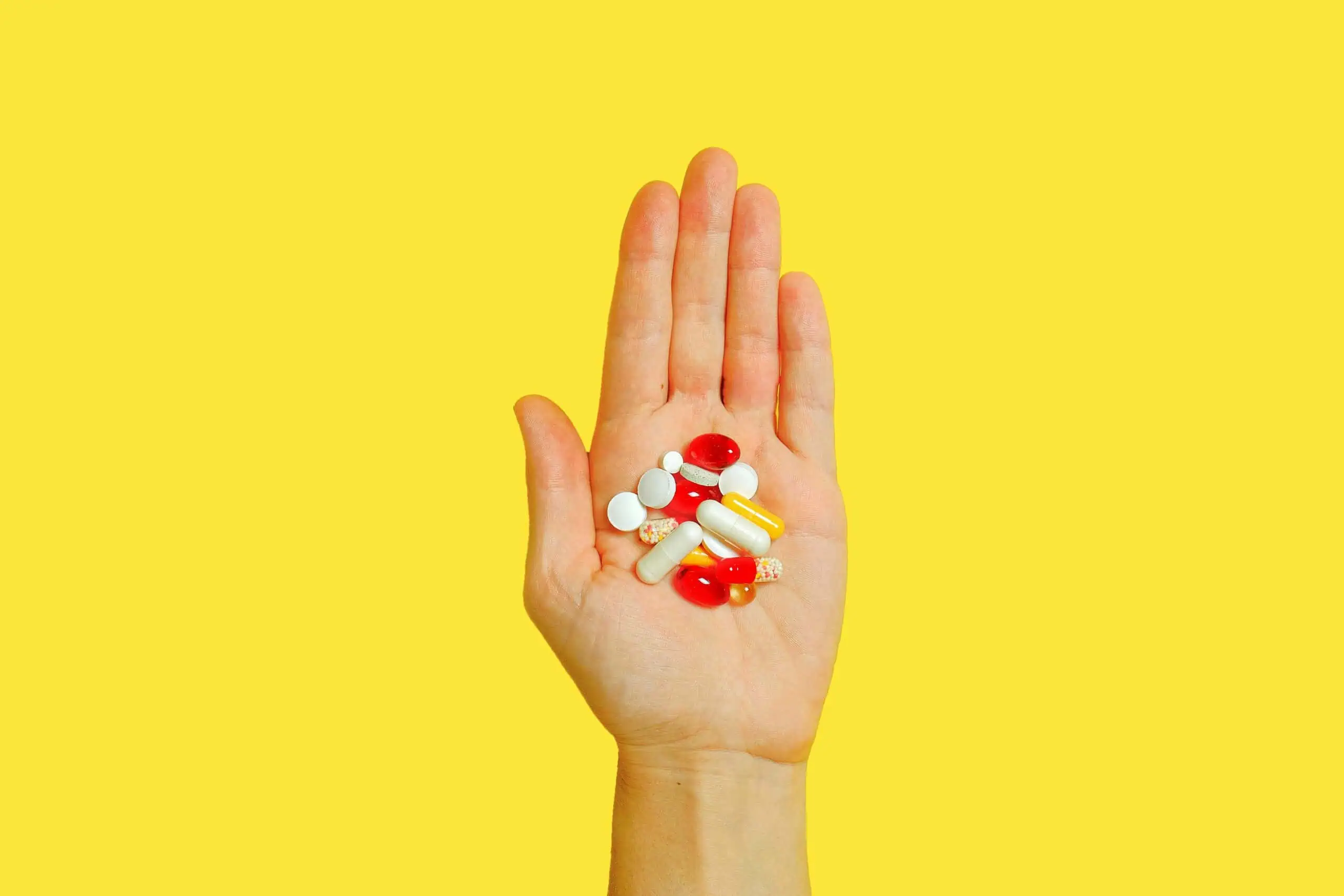 Outstretched and open hand with many medication pills on a yellow background
