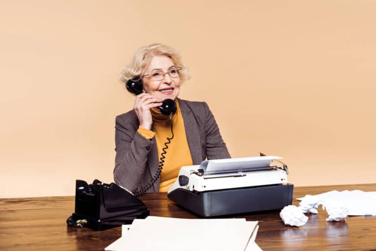 Stylish senior woman in eyeglasses talking on rotary phone at table