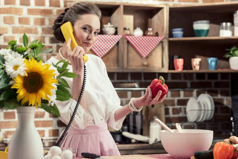 Smiling adult housewife talking by retro wired phone