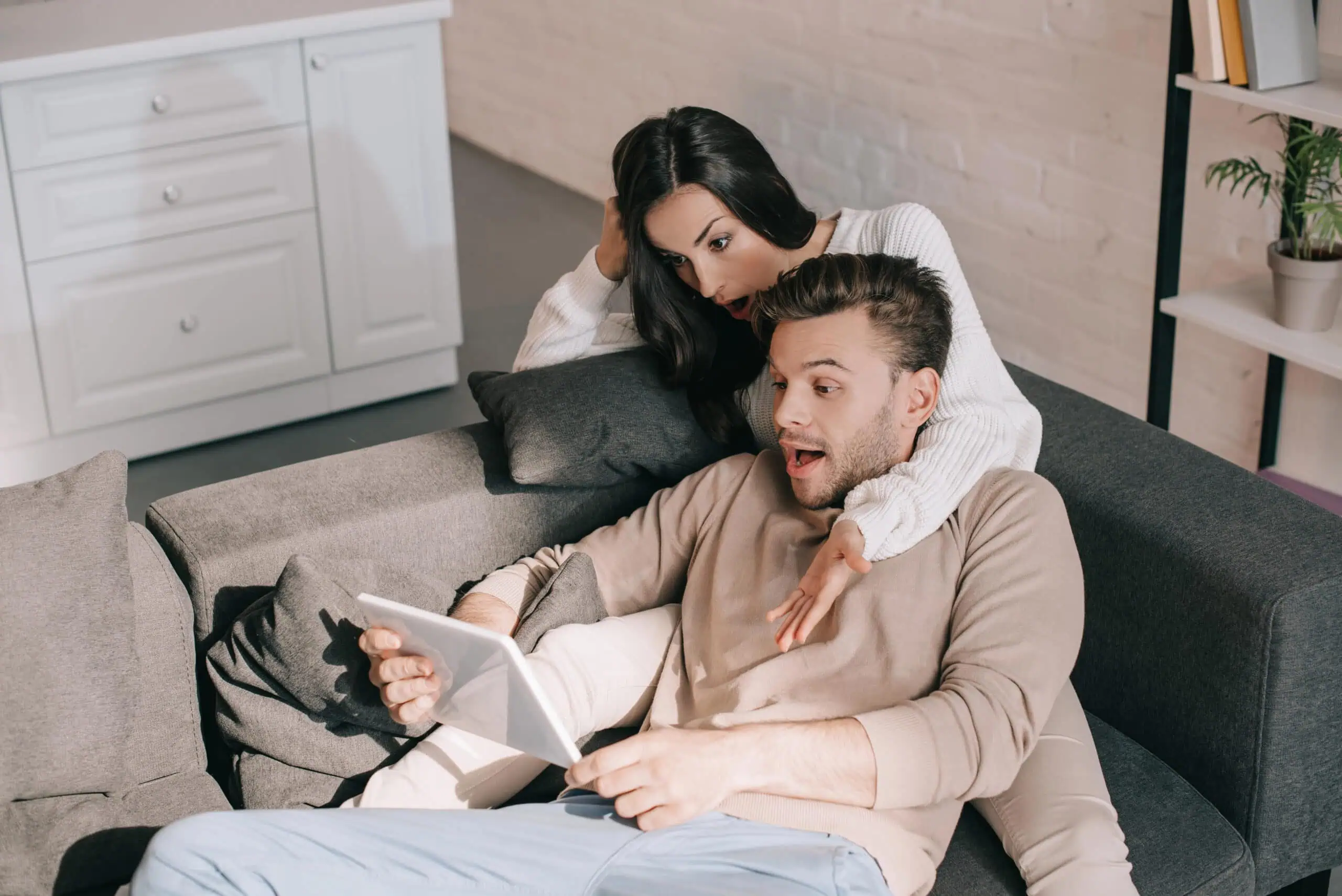 Shocked young couple using tablet together on couch at home
