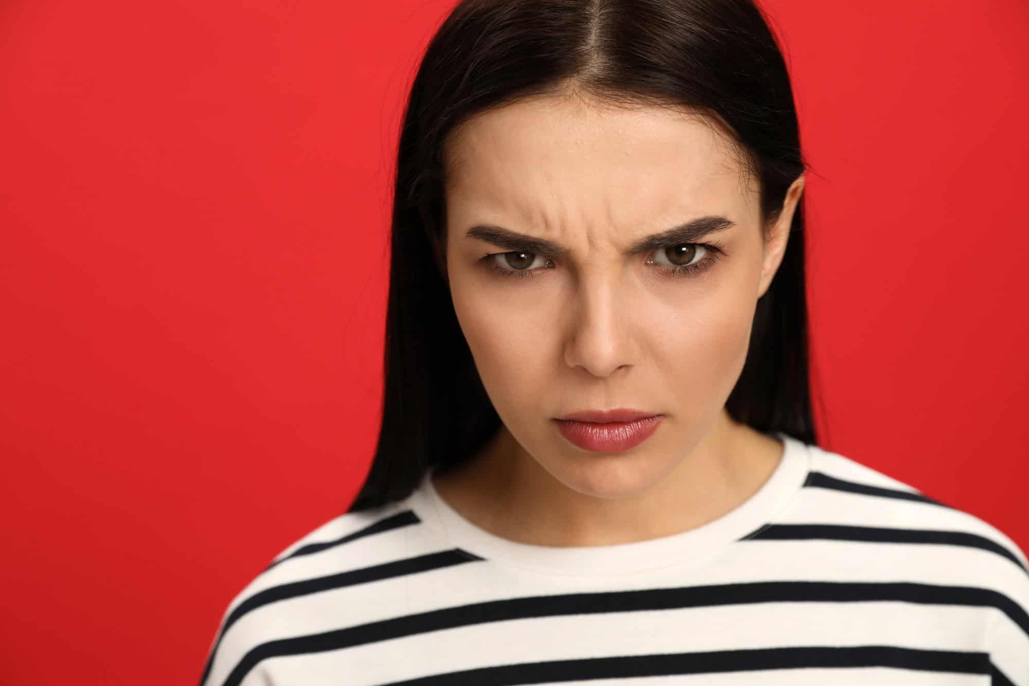 Angry young woman on red background. Hate concept