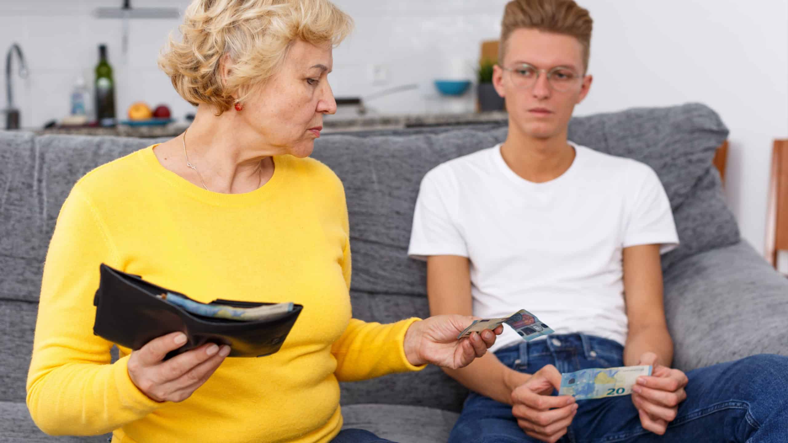 Senior woman giving money her adult son at kitchen