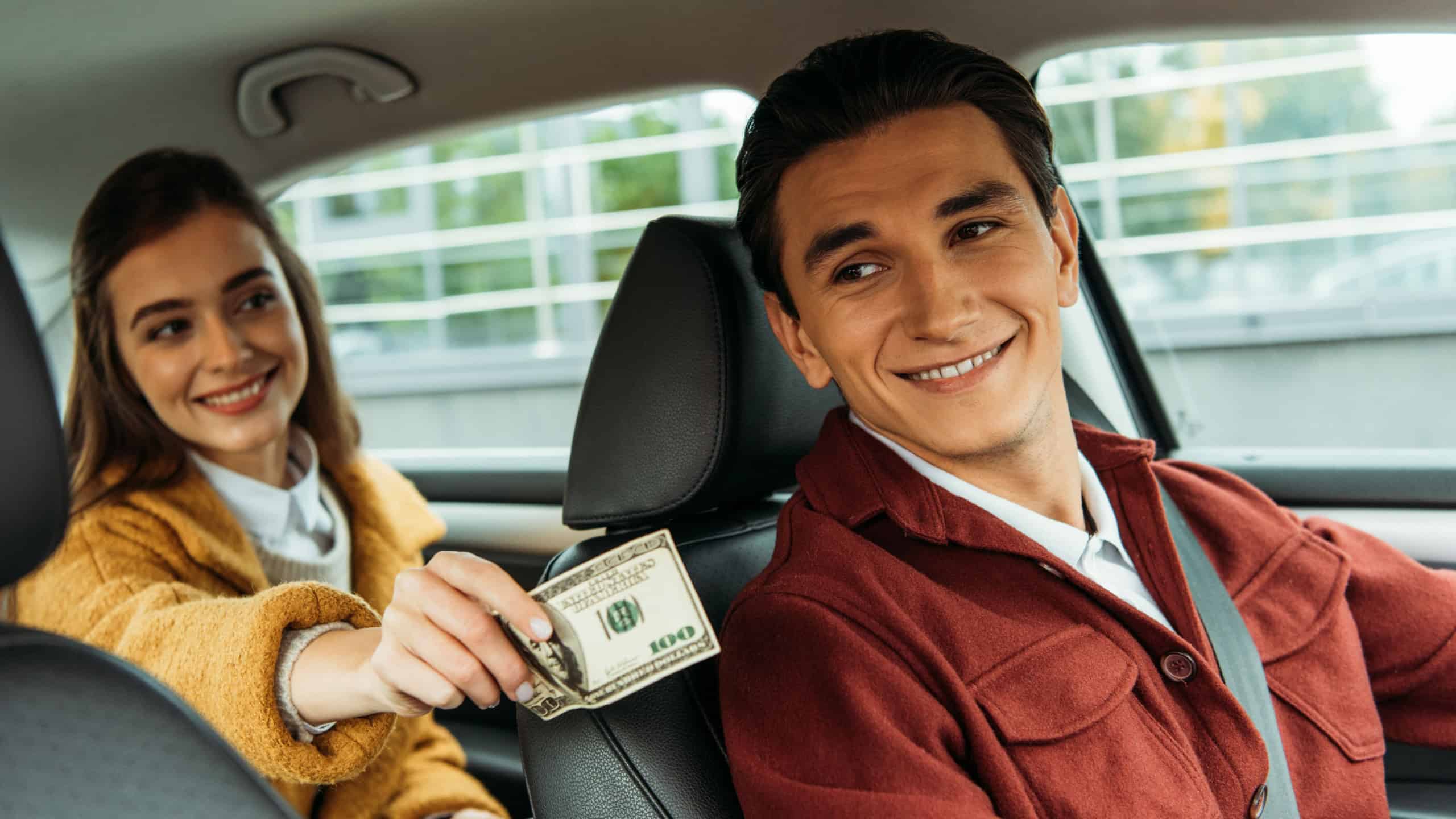 Smiling woman passenger giving cash to taxi driver