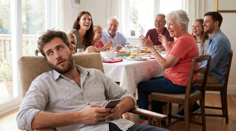 Image of an young adult man annoyed at a family gathering with his parents, grandparents and cousins.