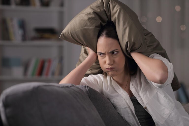 Angry homeowner suffering neighbor noise covering ears sitting on a couch in the night at home