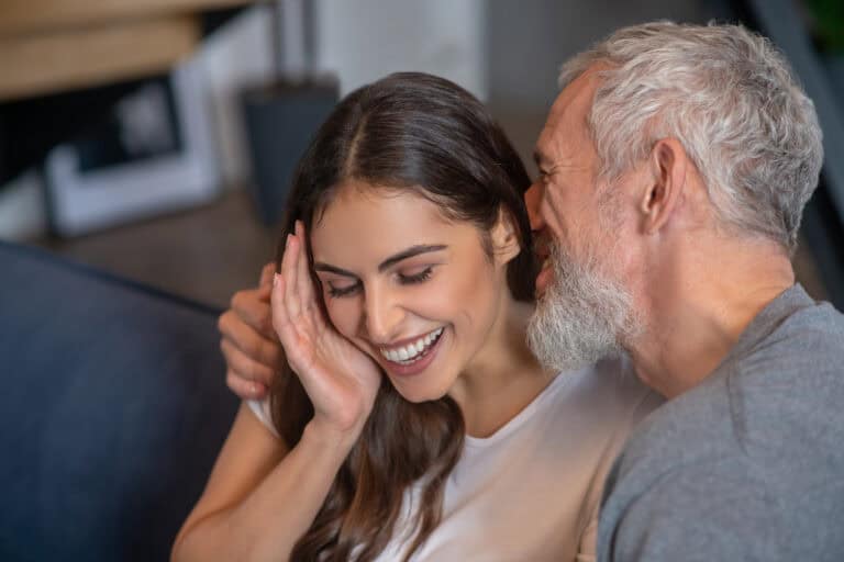 Happy together. A grey haired man saying compliments to his young spouse
