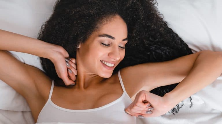 Young african happy cheerful woman in white pajamas waking up after sleeping, stretching and full of energy to start new day in the morning in the hotel room