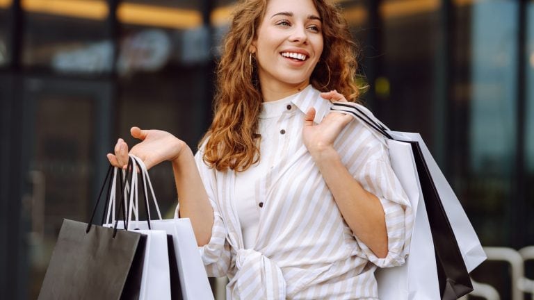 Shopping time. Young woman walking down with shopping bags on city street. Consumerism, purchases, black friday, lifestyle, sale concept.