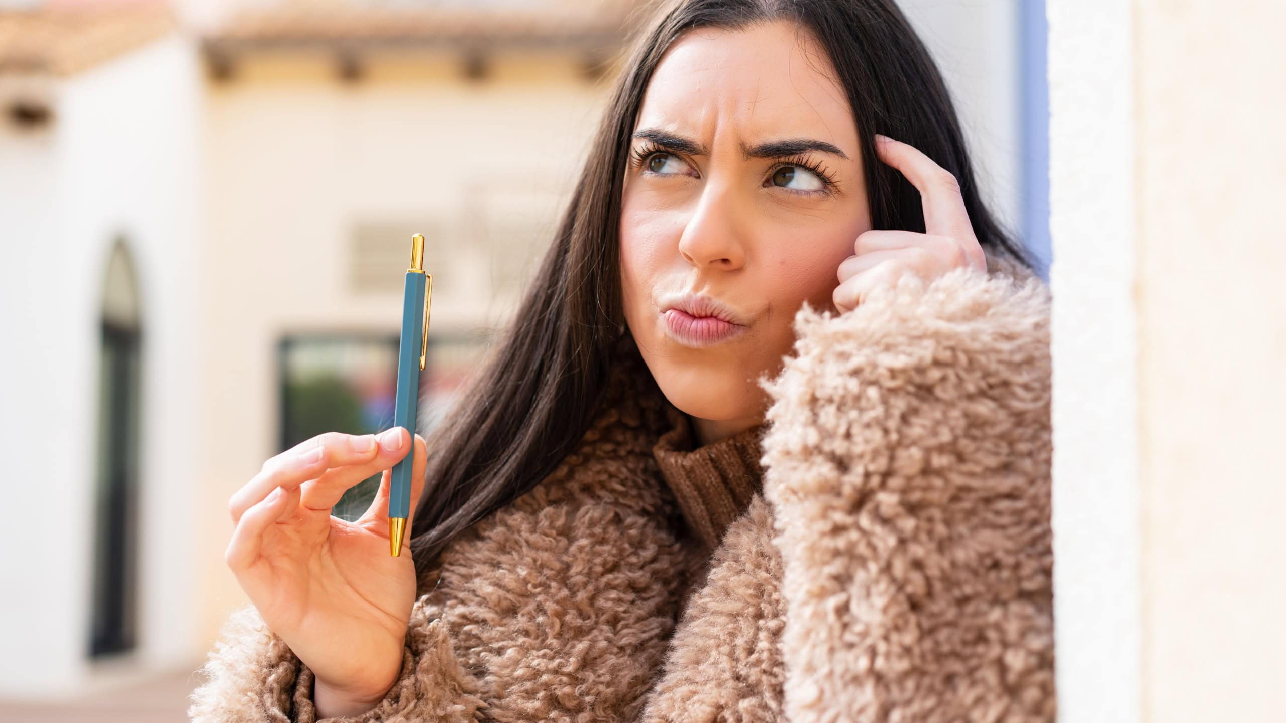 Young woman holding a pen at outdoors having doubts and with confuse face expression