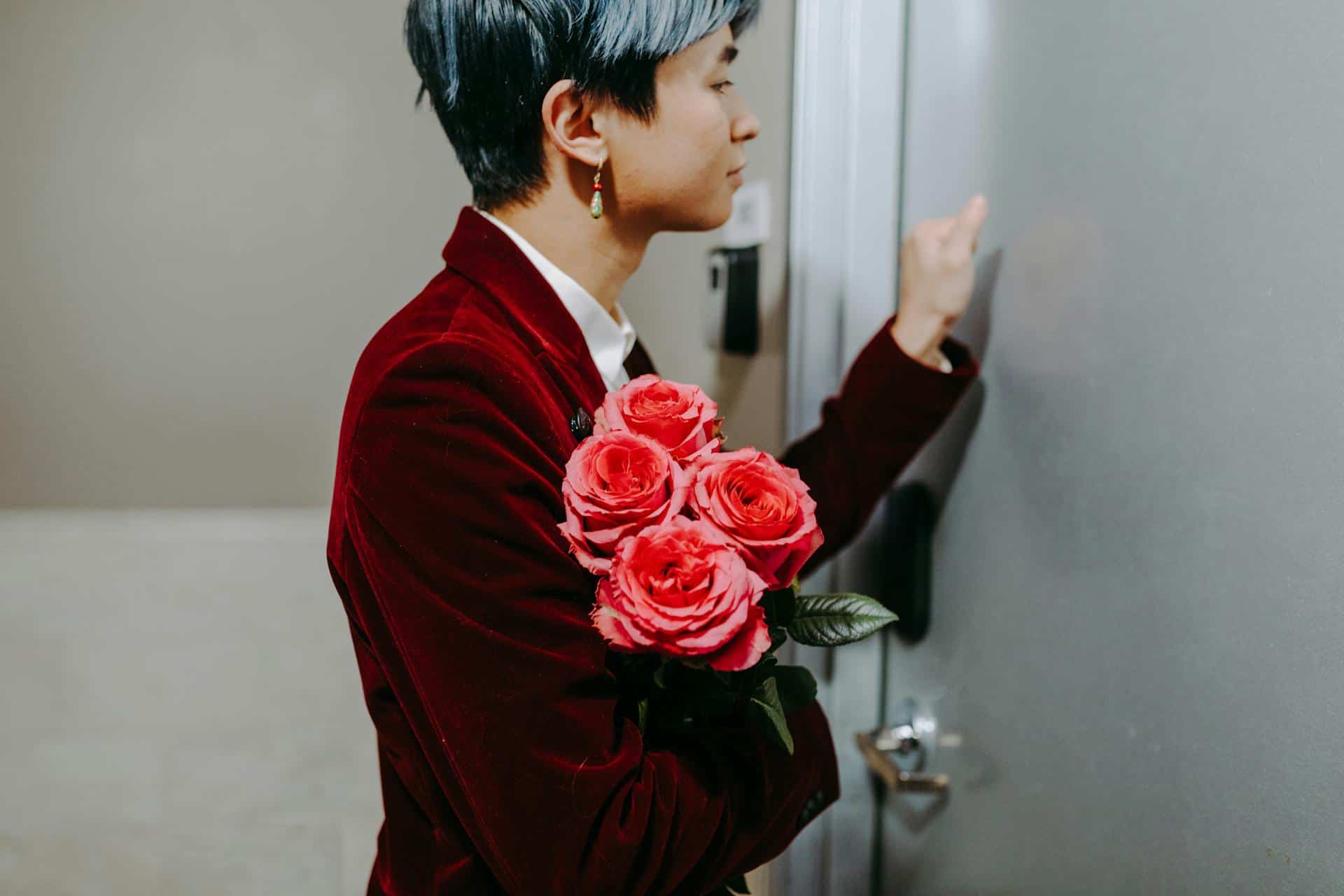 A Man in Red Suit Holding a Red Roses while Knocking on the Door