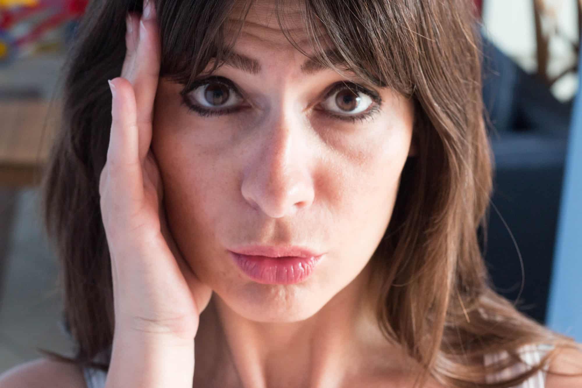 close up portrait of caucasian young woman with long hair and bangs. guilty Expression.