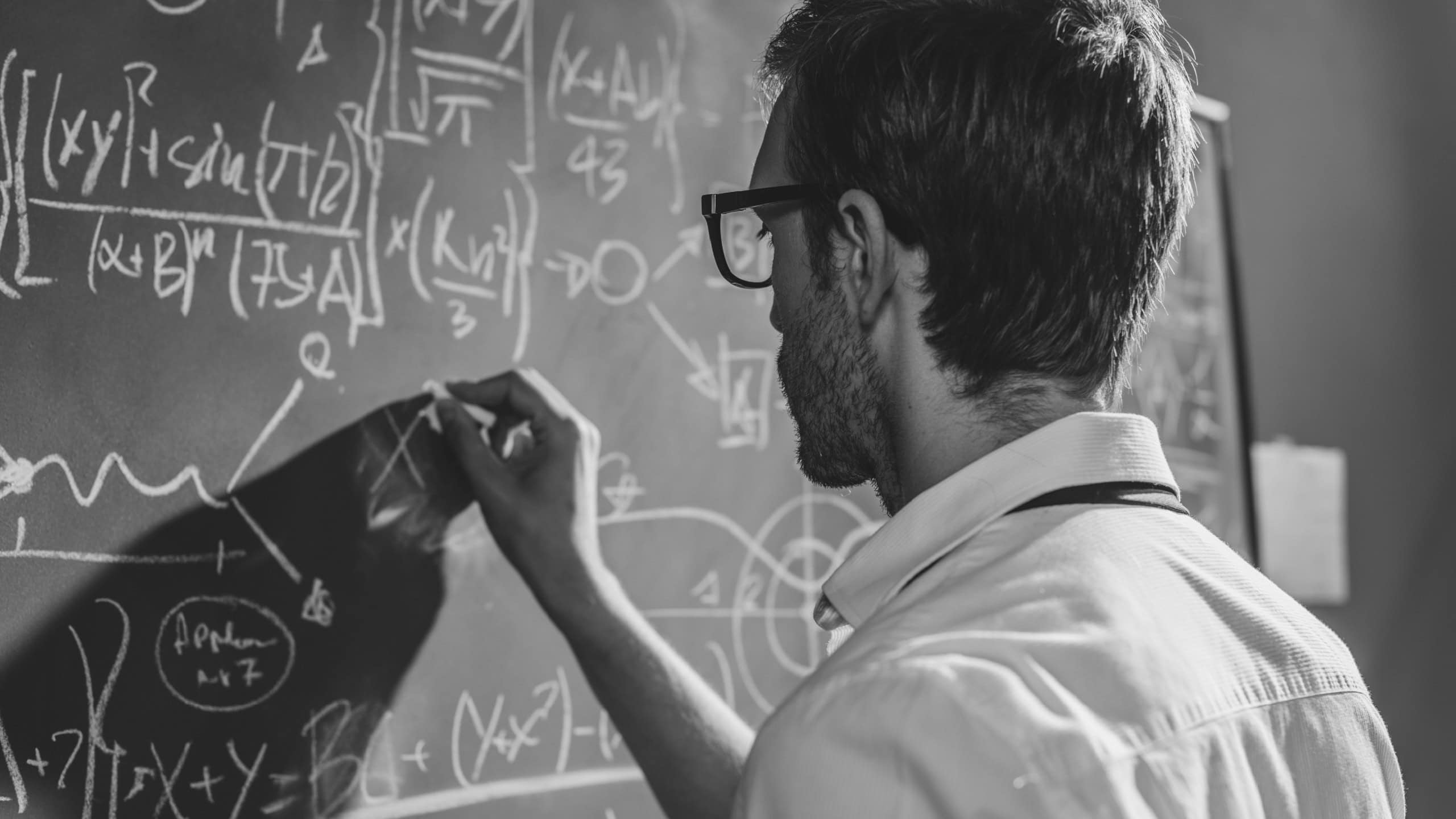 Young smart mathematician drawing math formulas on the chalkboard and thinking: he is solving problems and discovering new theories