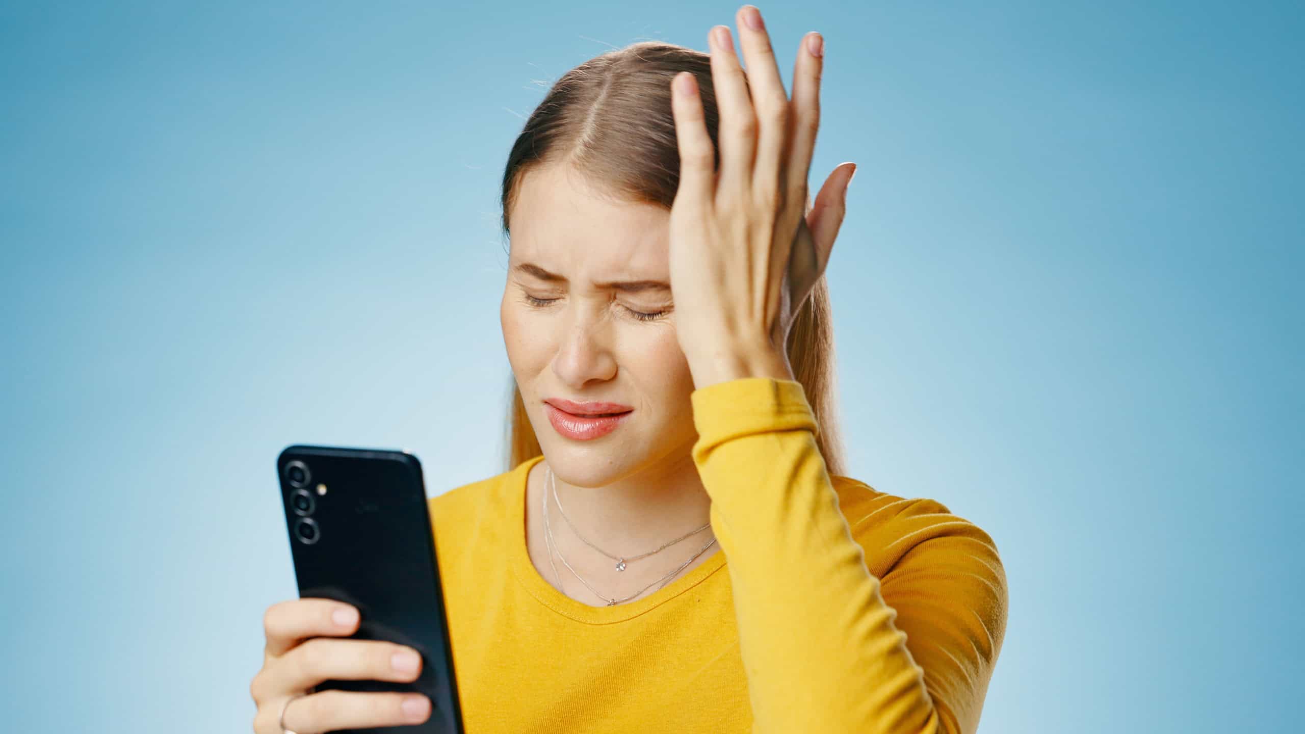 Cellphone, studio and woman with headache, hurt and brain fog on blue background. Technology, hand and pain for expression with smartphone for medical research, internet and online information