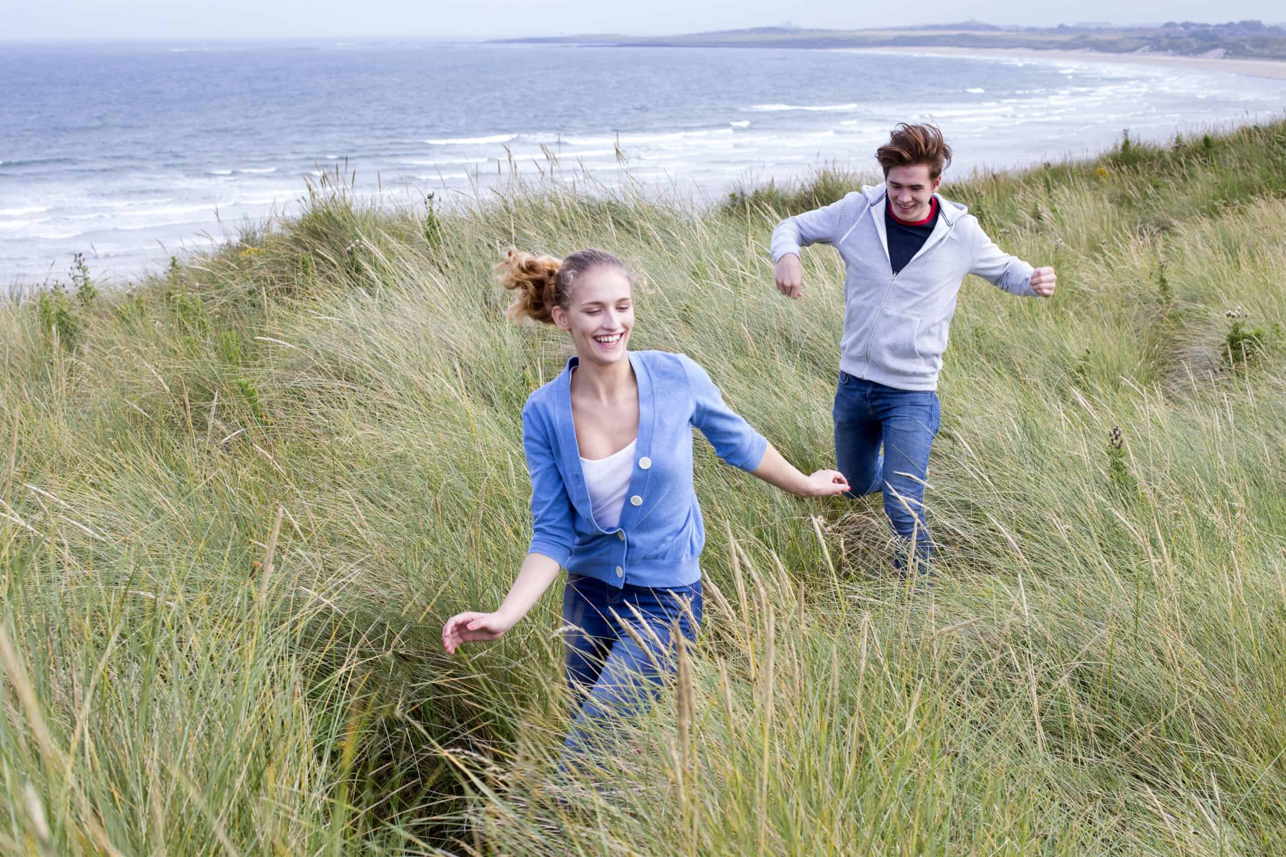 Couple running through grass, laughing and smiling