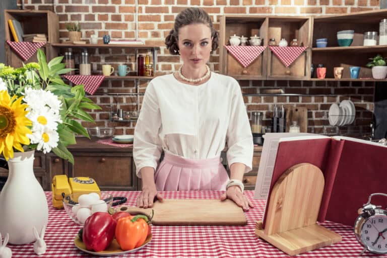 Serious adult housewife in vintage clothes looking at camera at kitchen
