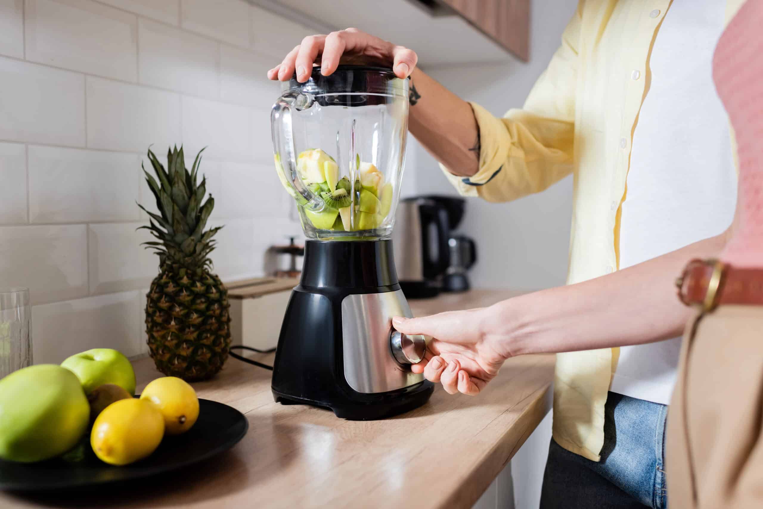 Cropped view of woman switching blender with fruits near husband in kitchen