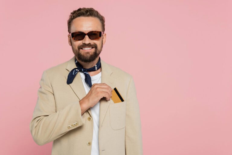 Happy man in stylish sunglasses and neck scarf putting credit card in pocket