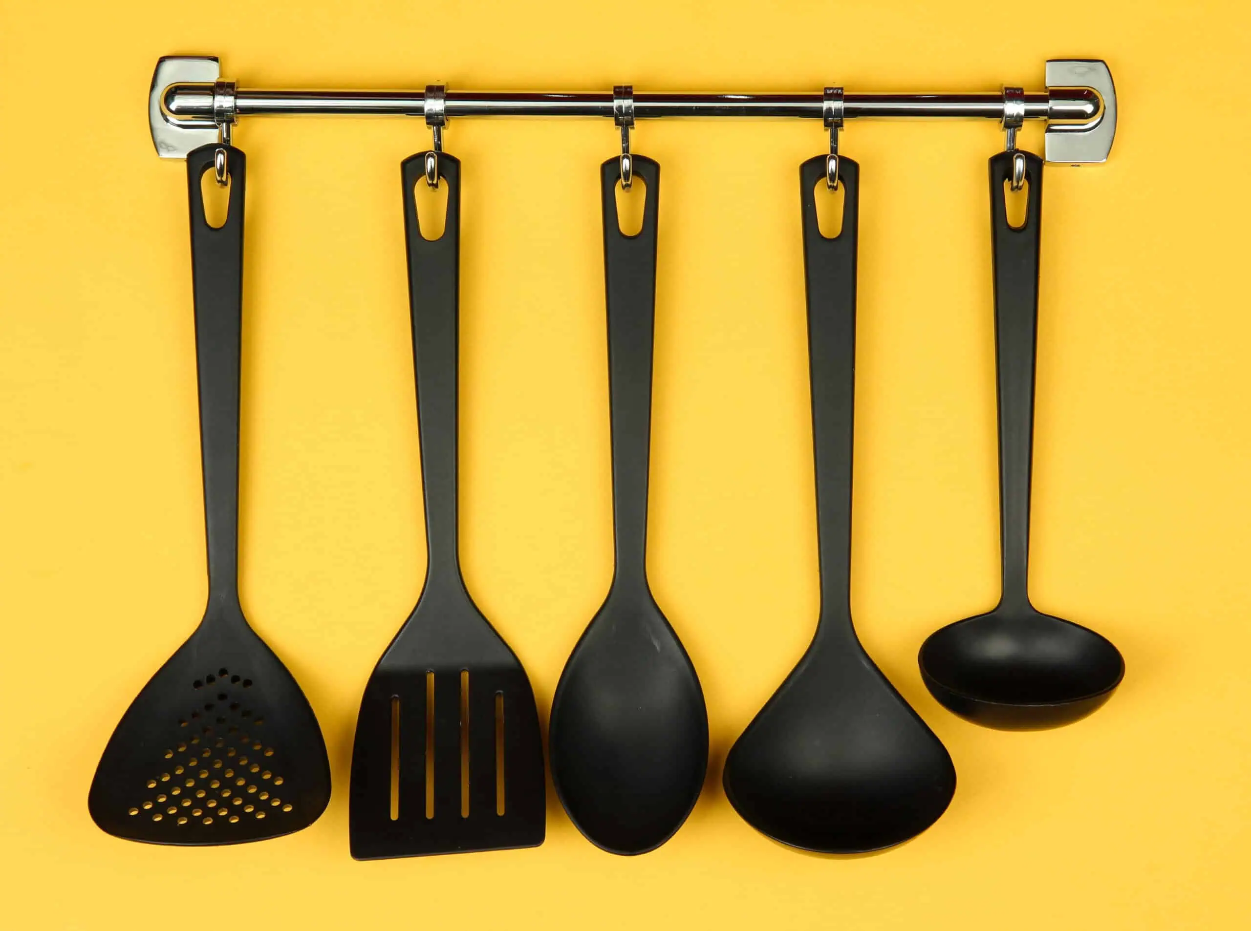 Black kitchen utensils on silver hooks, on yellow background