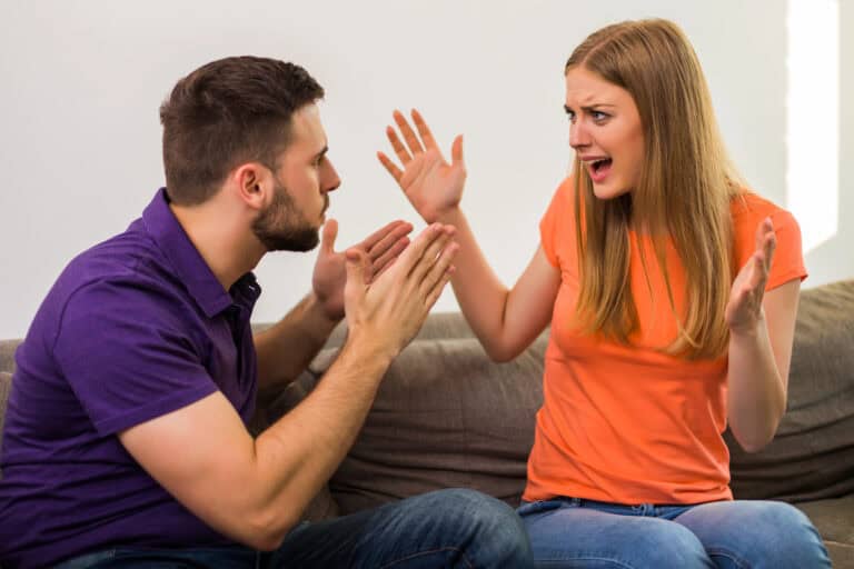 Angry wife and husband are having conflict while they sitting on sofa at their home.