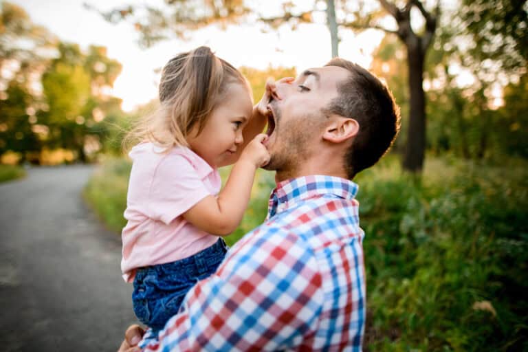 Little girl sits in her fathers arms and carefully looks into his mouth
