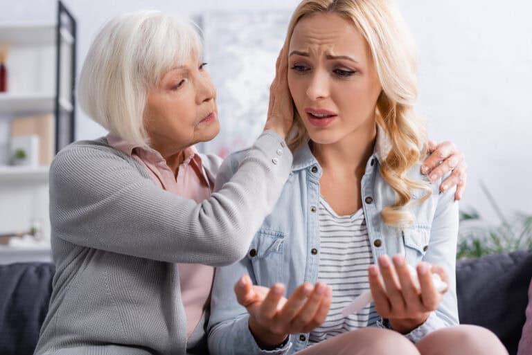 Elderly mother calming displeased daughter with napkin at home