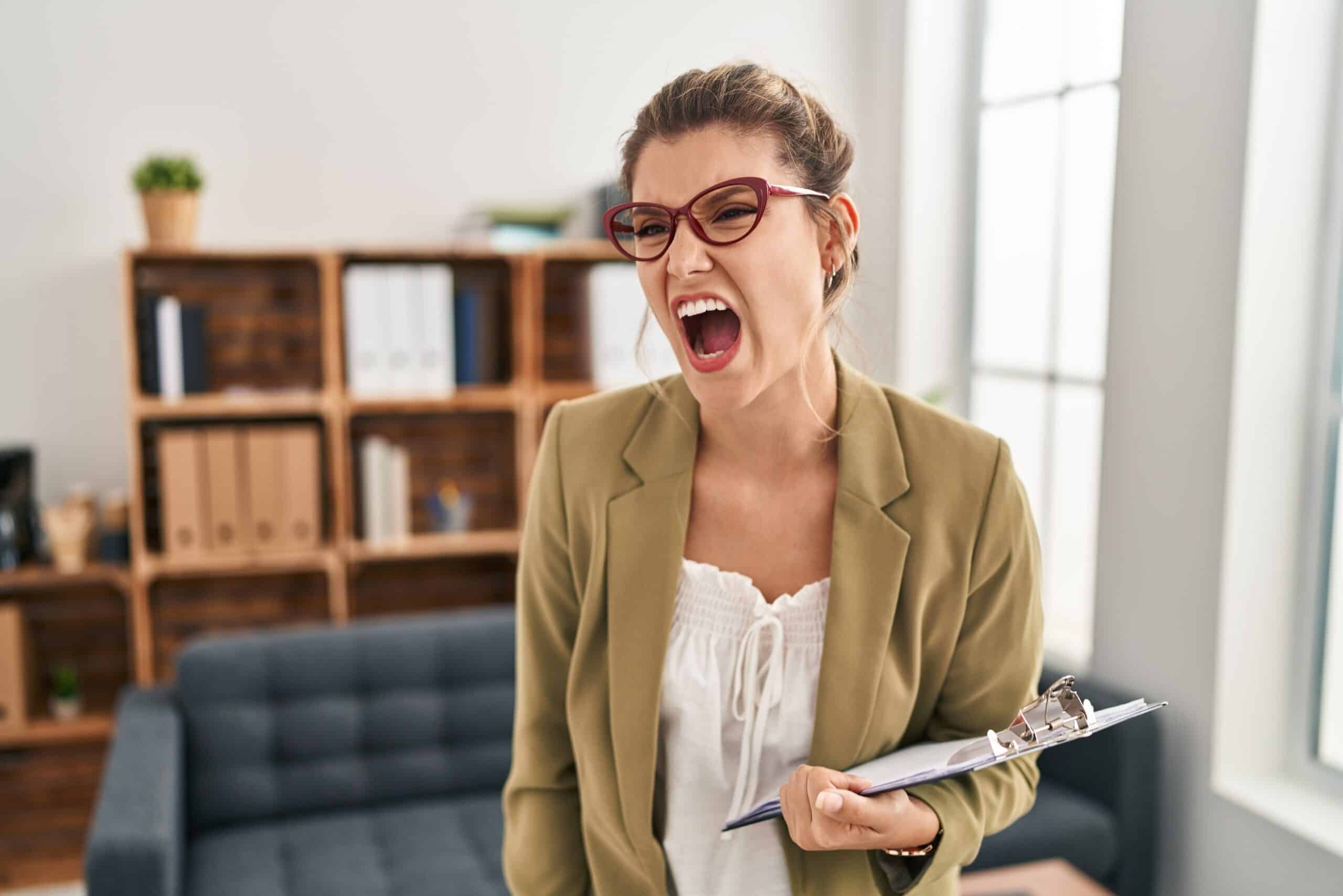 Young woman working at consultation office angry and mad screaming frustrated and furious, shouting with anger. rage and aggressive concept.
