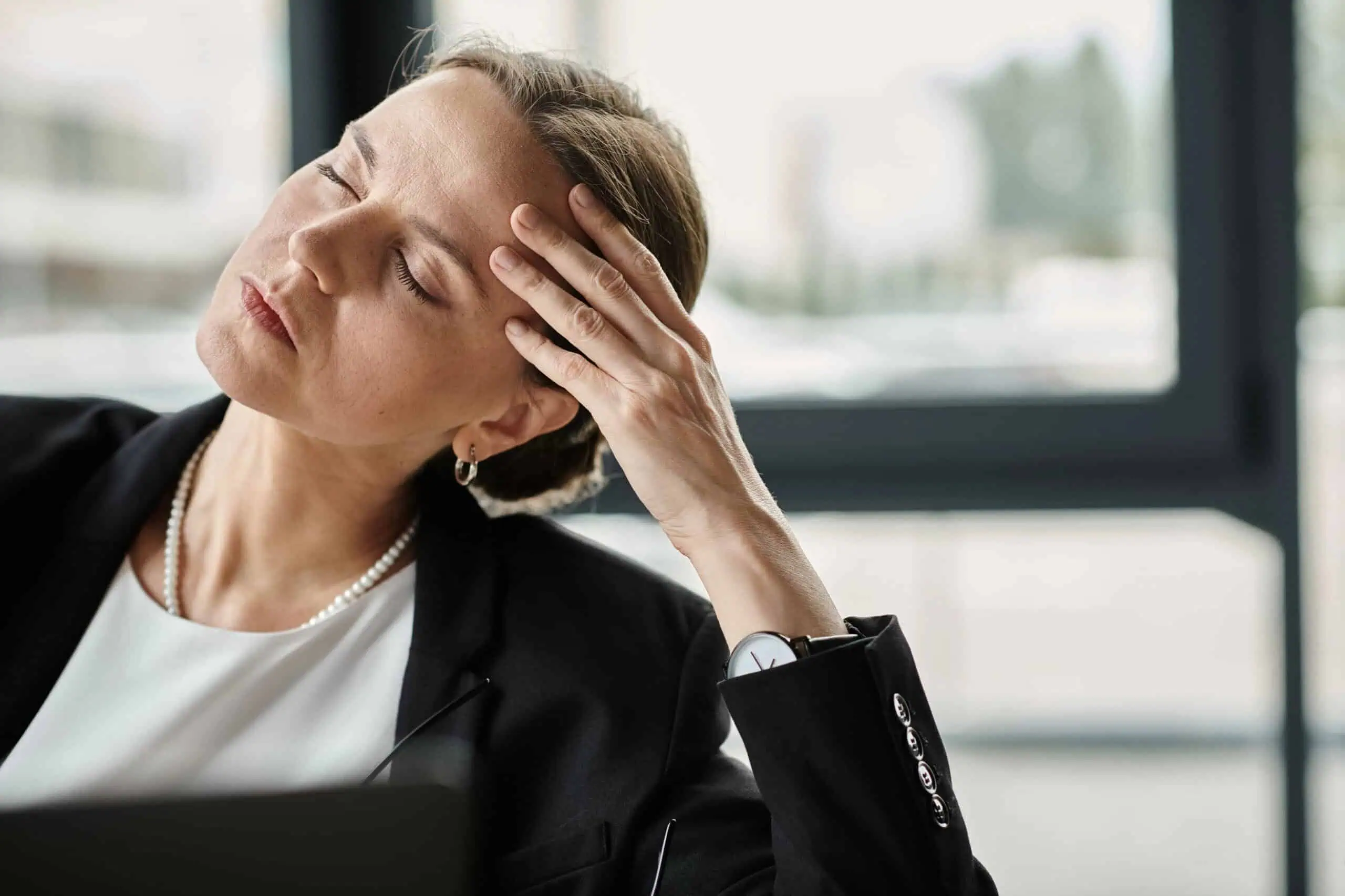 Middle aged woman in business suit holds head while working