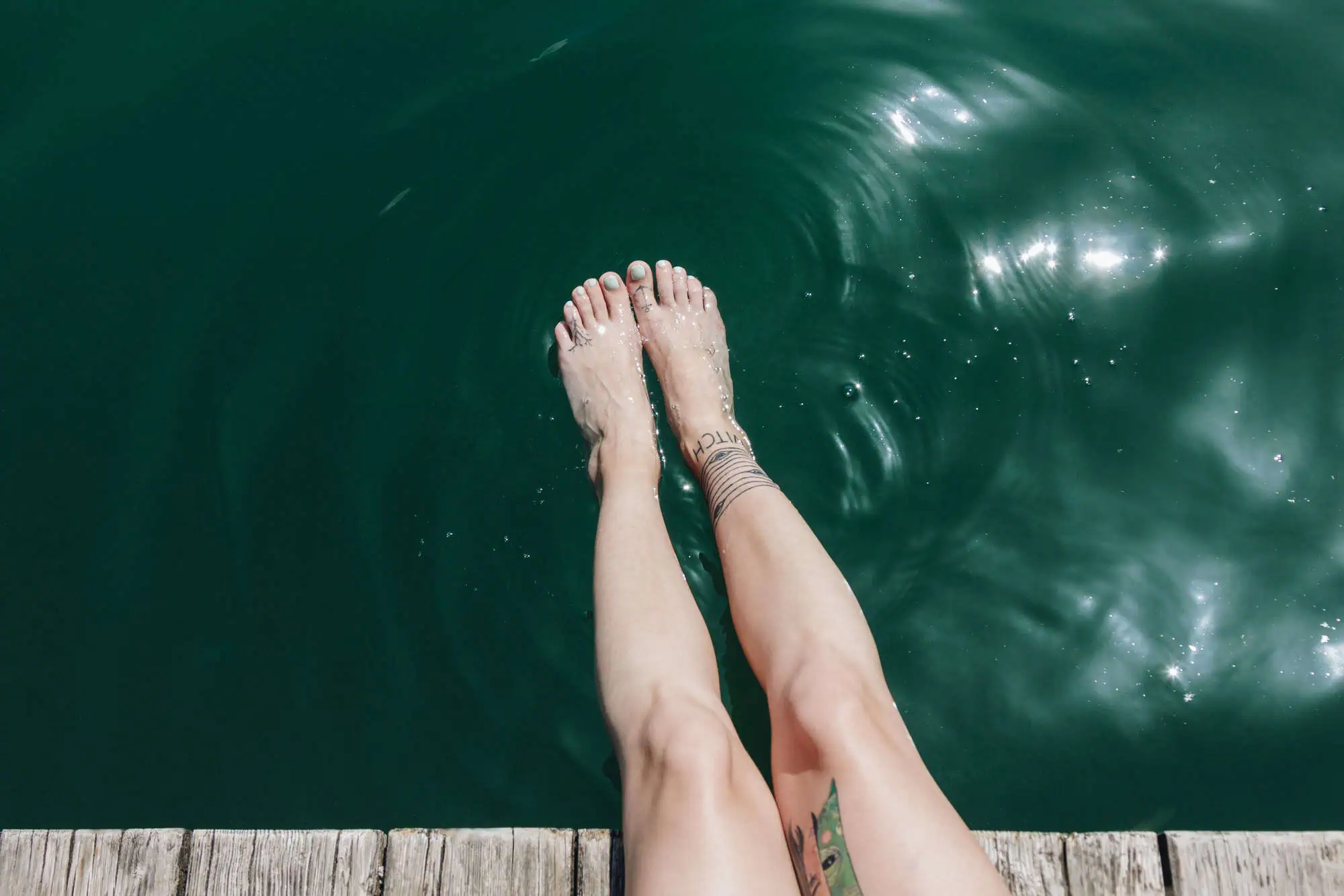 Cropped shot of female legs with tattoos in calm water at sunny day