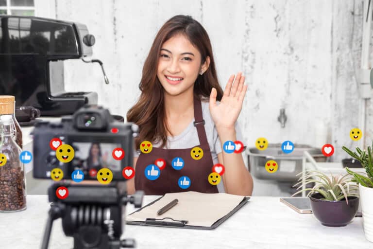 Portrait of happy beauty asian business startup owner barista vlogger woman relax use camera technology online marketing communication recording video content for live stream chat with icon online social media at cafe