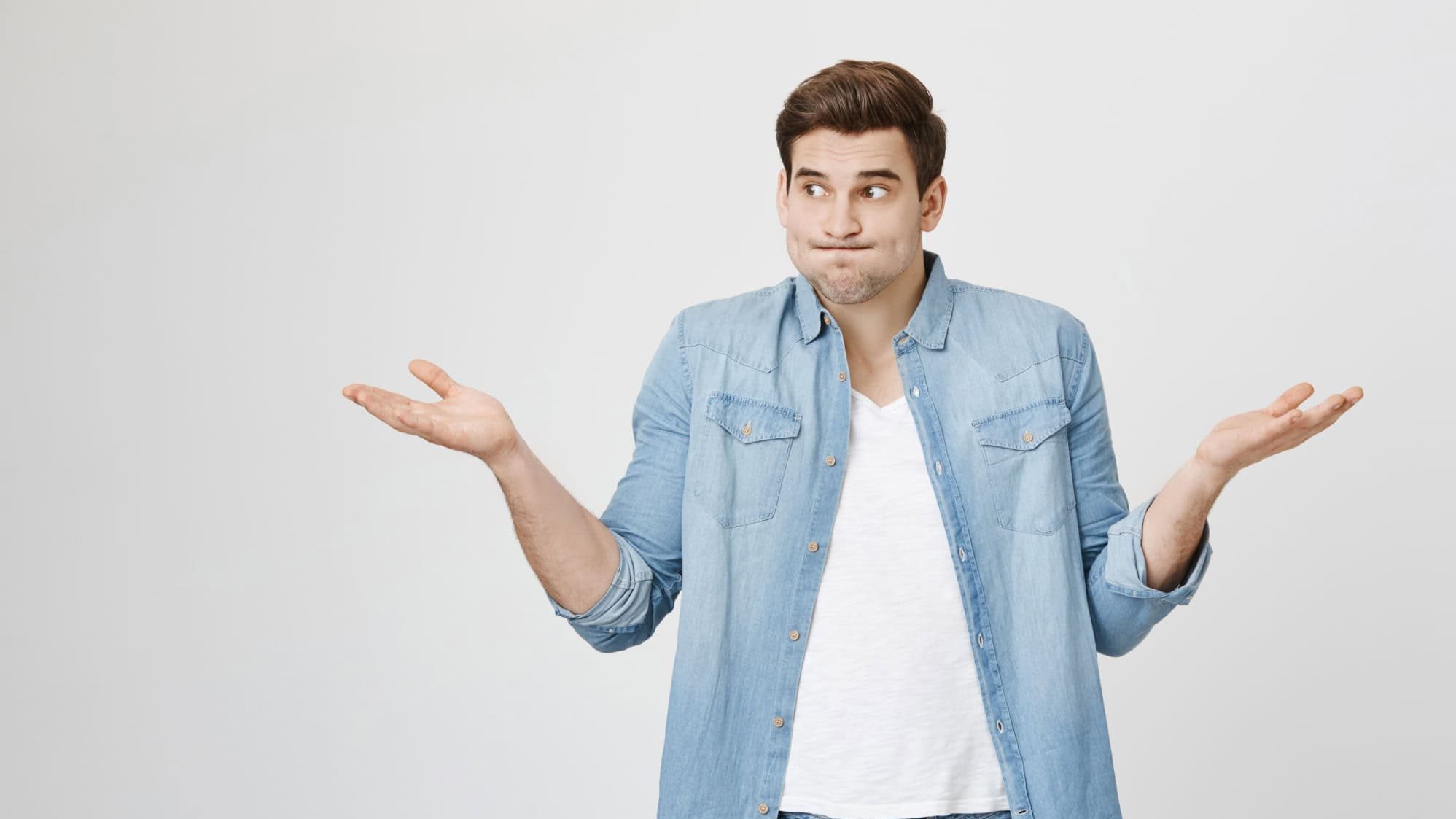 Portrait of funny handsome guy, shrugging and spreading hands, expressing unknowladge and confusion, widen eyes, standing over gray background. I do not know what are you talking about