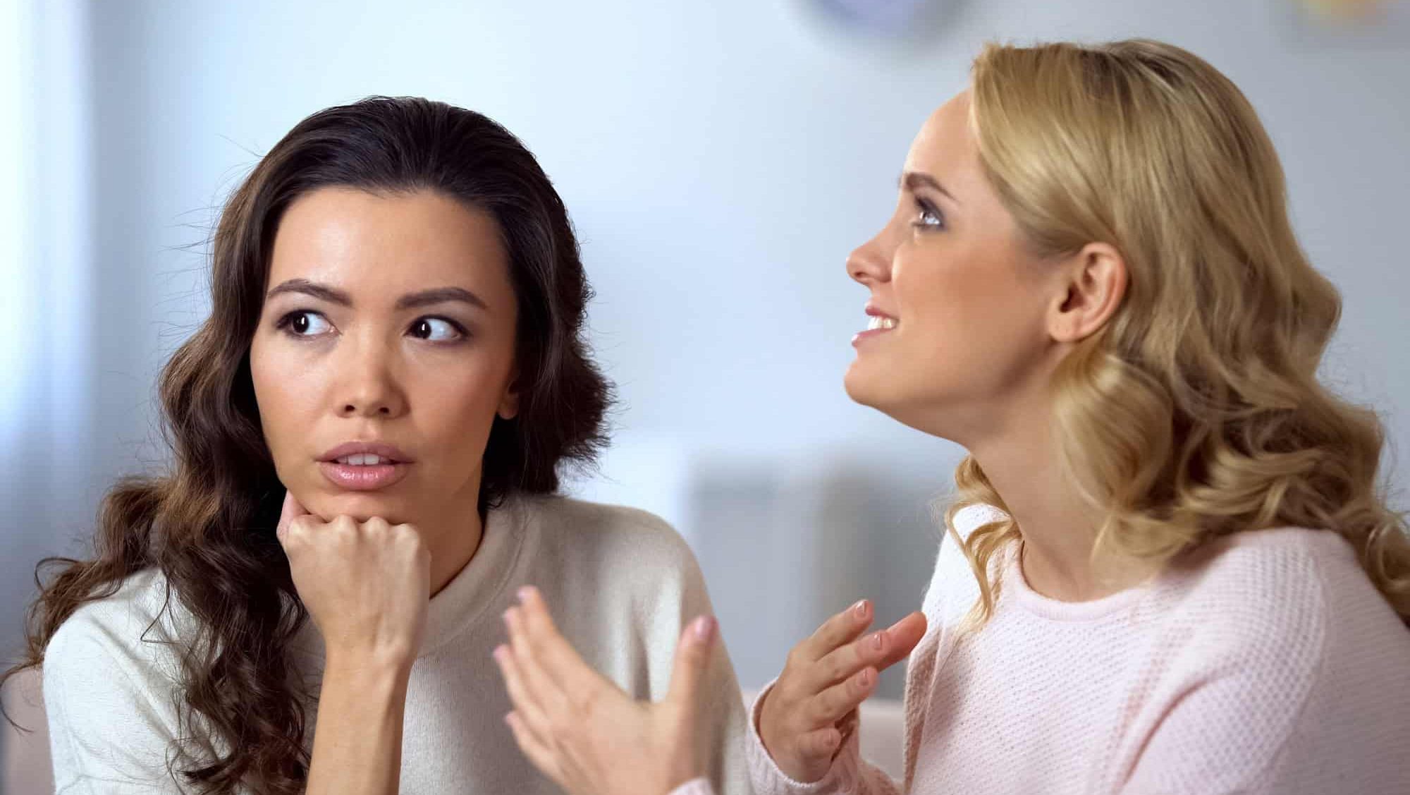Bored Asian woman listening her annoying friend, uninvolved in conversation