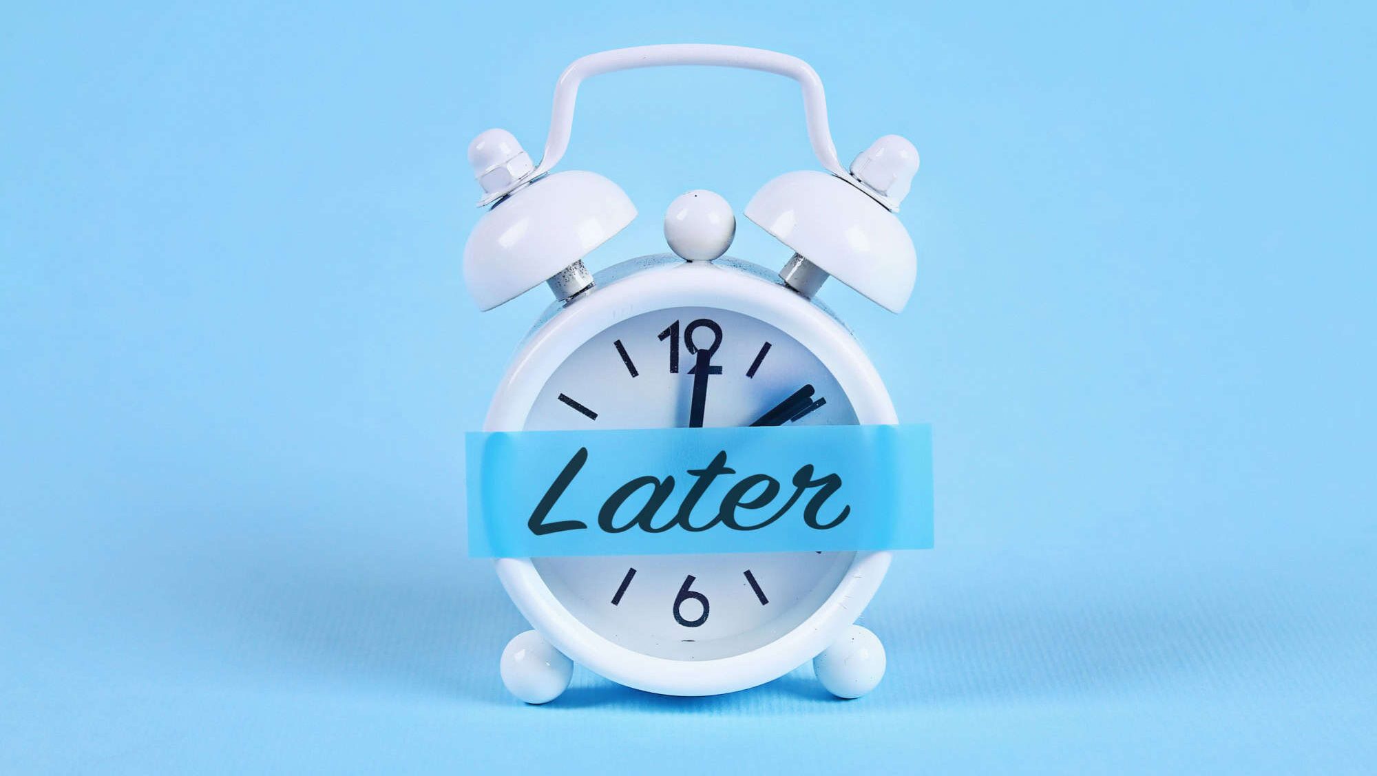 Procrastination, delay and urgency concept. White alarm clock with a sticky note with text later.