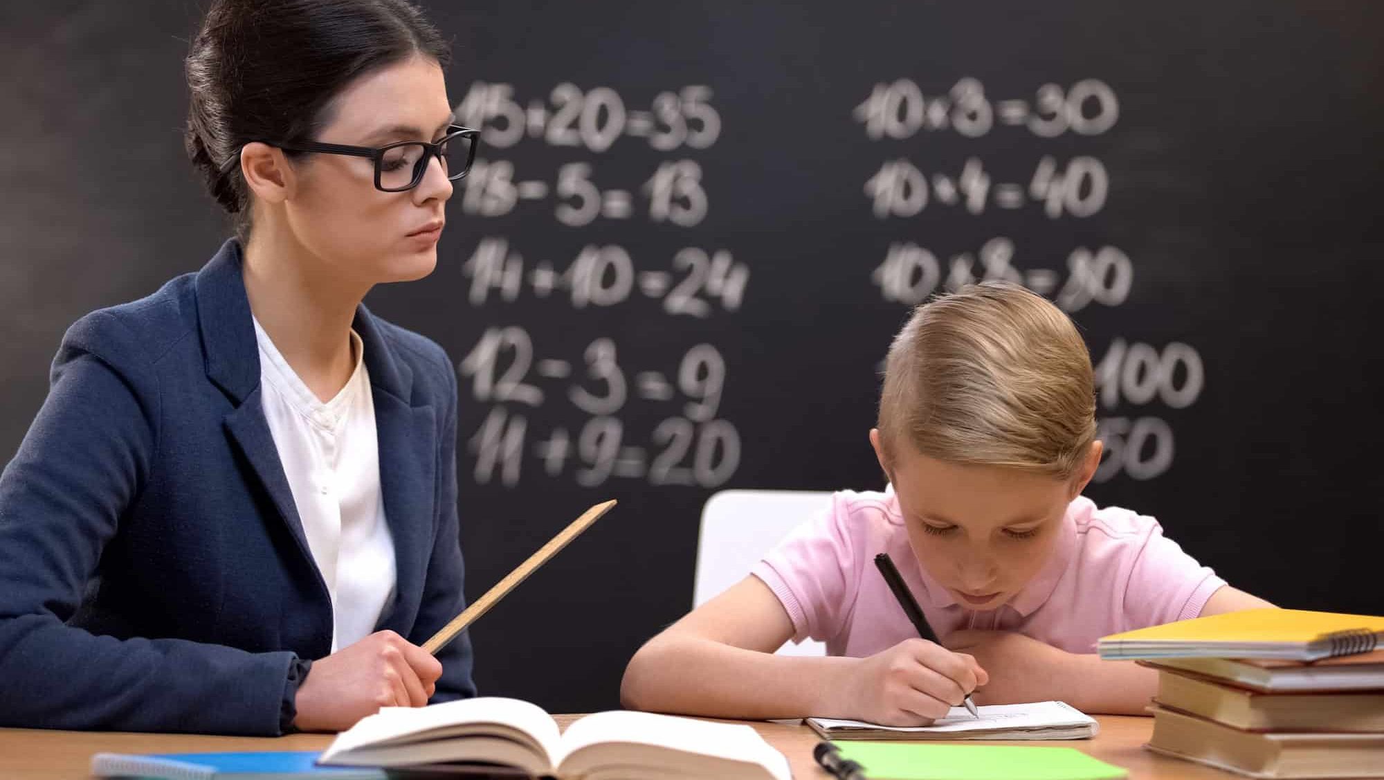 Strict teacher with ruler watching schoolboy doing his homework, control