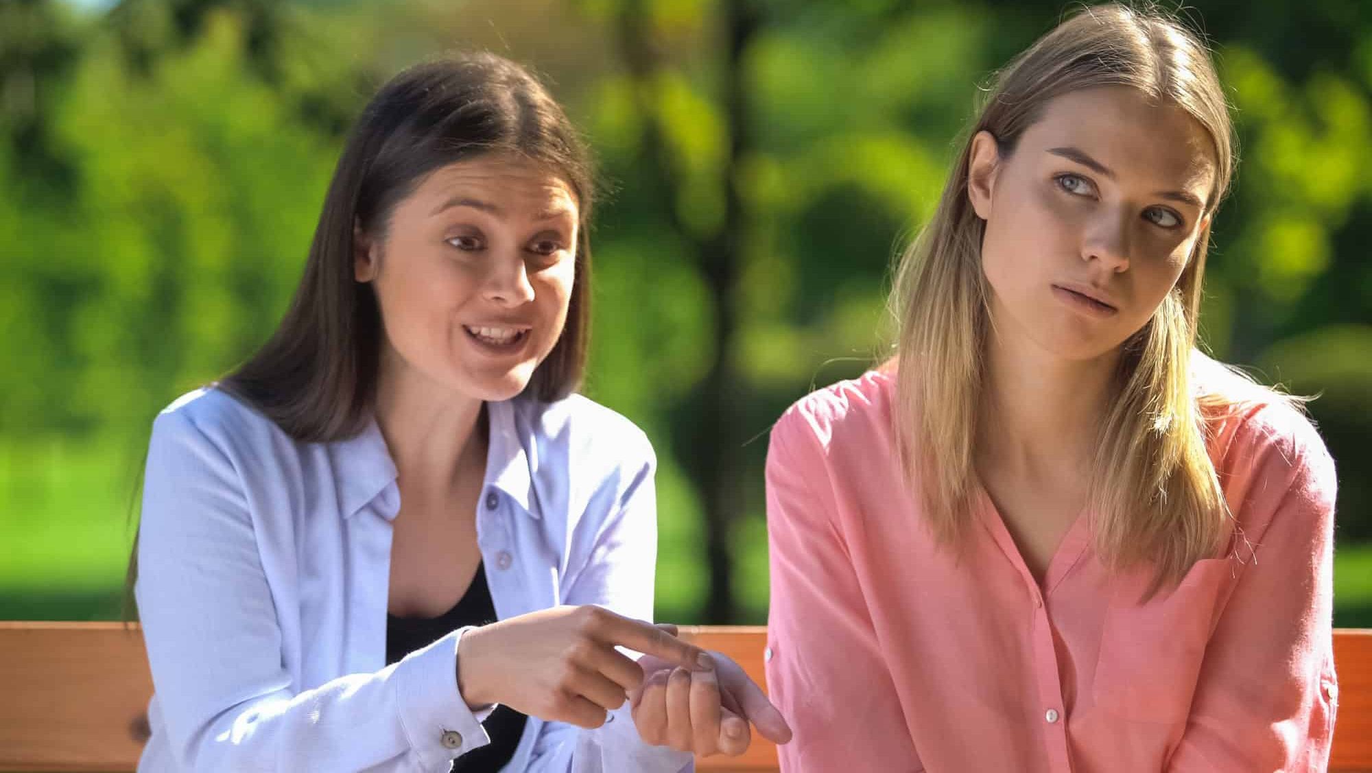 Tired female listening to annoying friend sitting outdoors, envy, selfishness