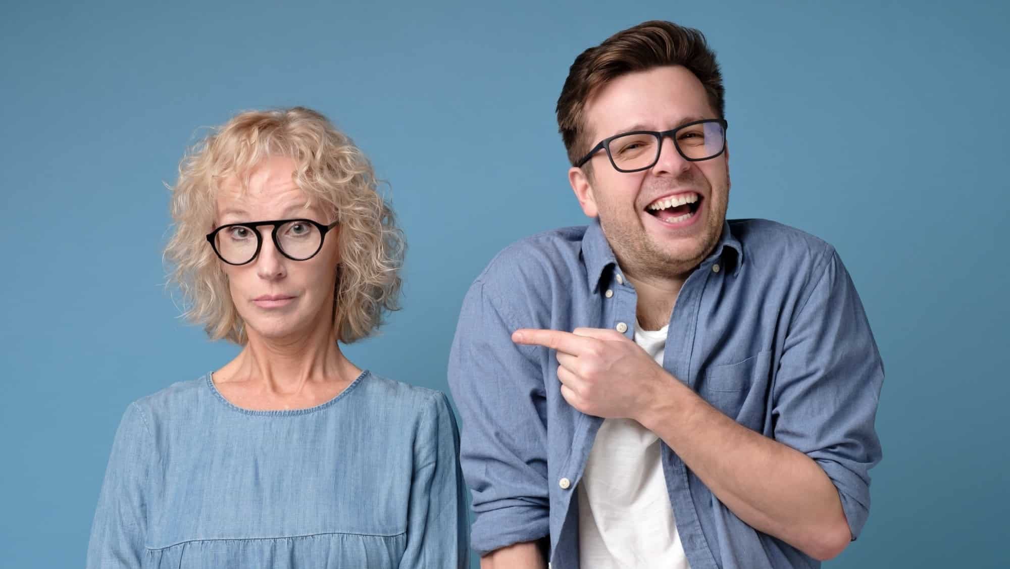 Cheerful handsome man laughing at his annoyed mature coworker