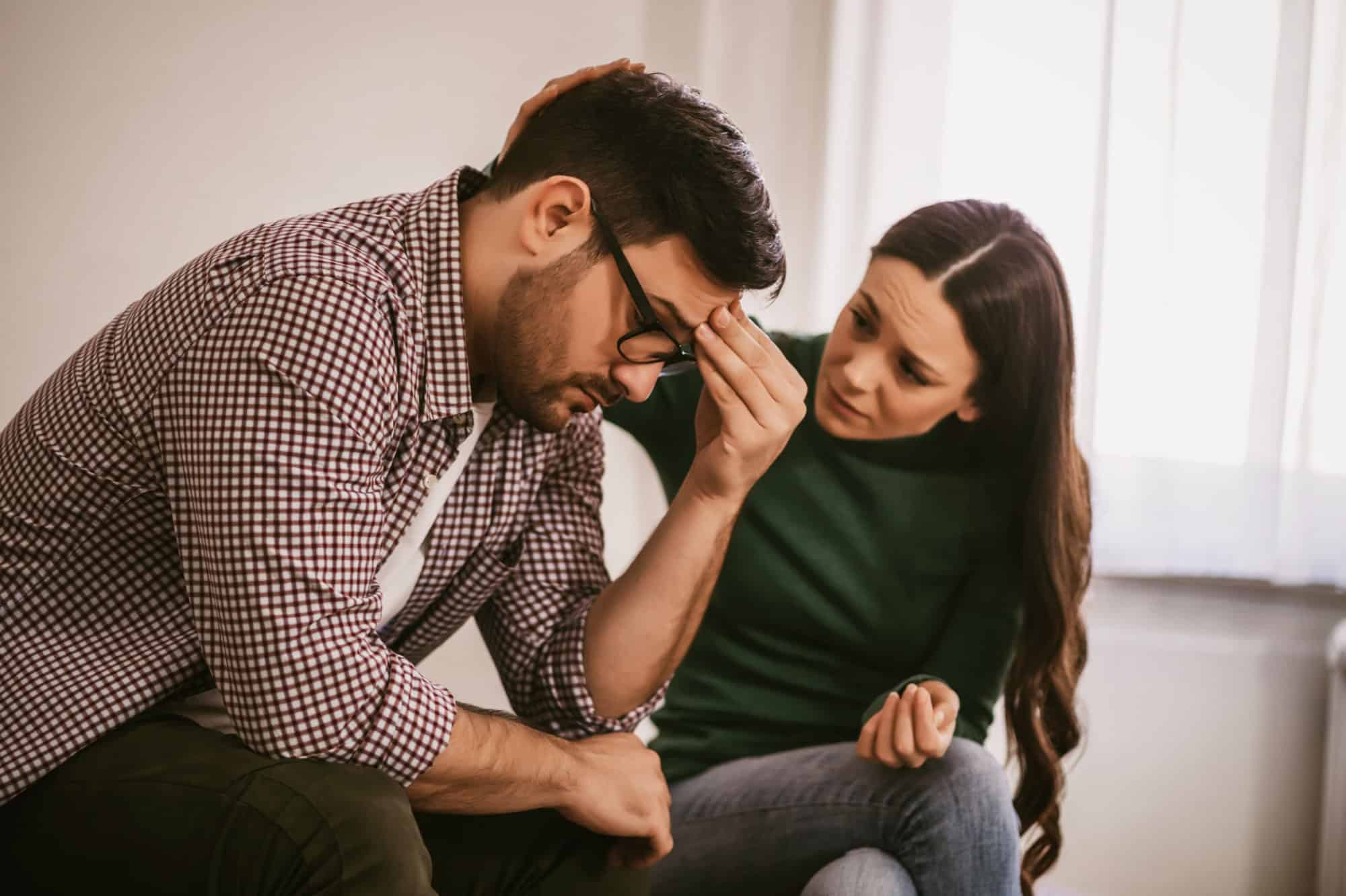 Man is sad and depressed, his wife is consoling him.