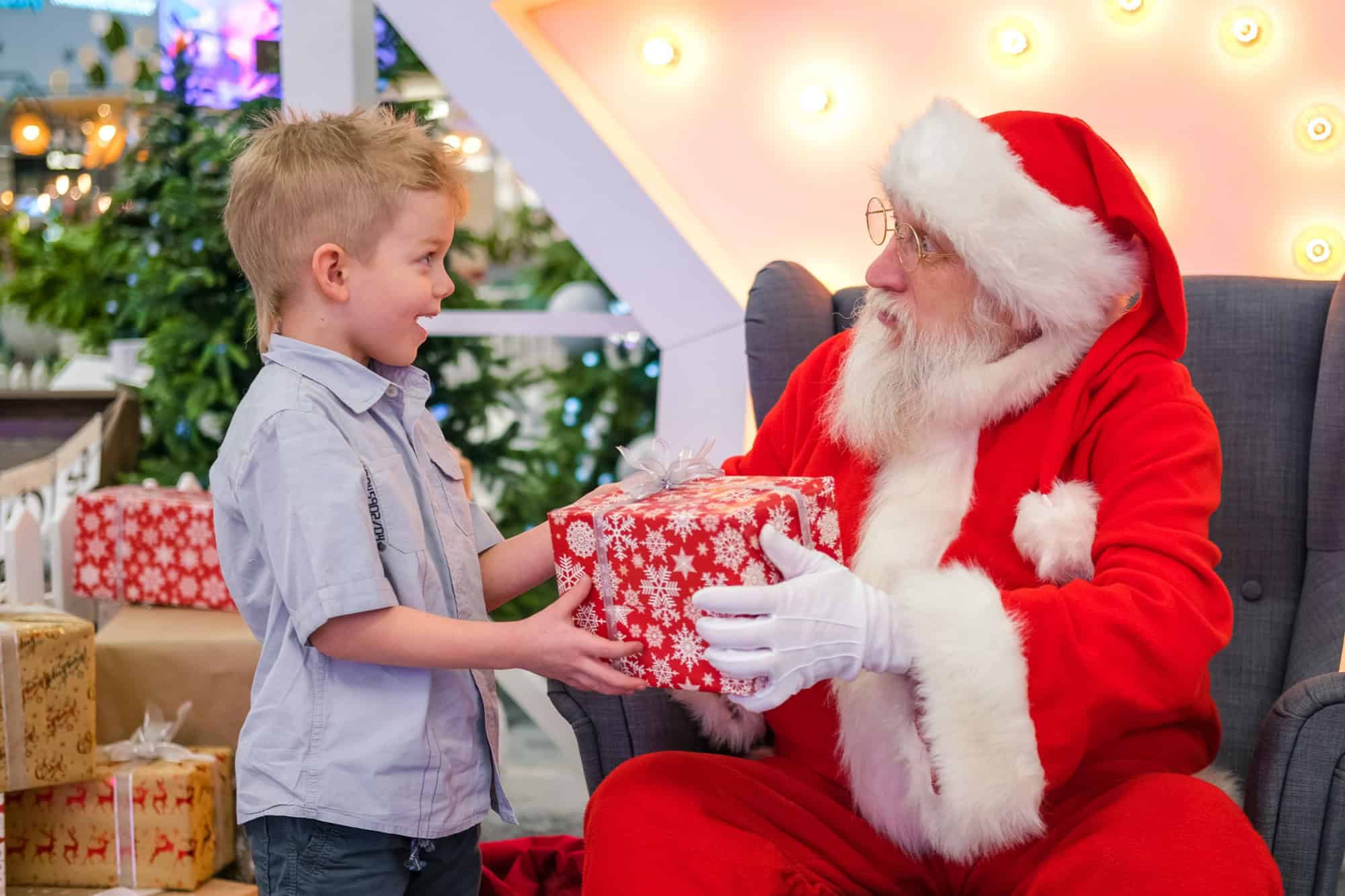 Santa Claus gives boy a gift in Shopping Mall. Real authentic Santa talking and playing surprise games with kids . Christmas sales and wishes.