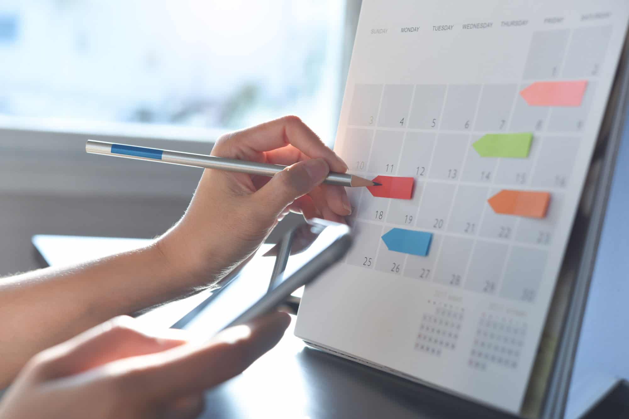 2025 Event planner timetable agenda plan on schedule event. Business woman checking planner on mobile phone, taking note on calendar desk on office table. Calendar event plan, work planning