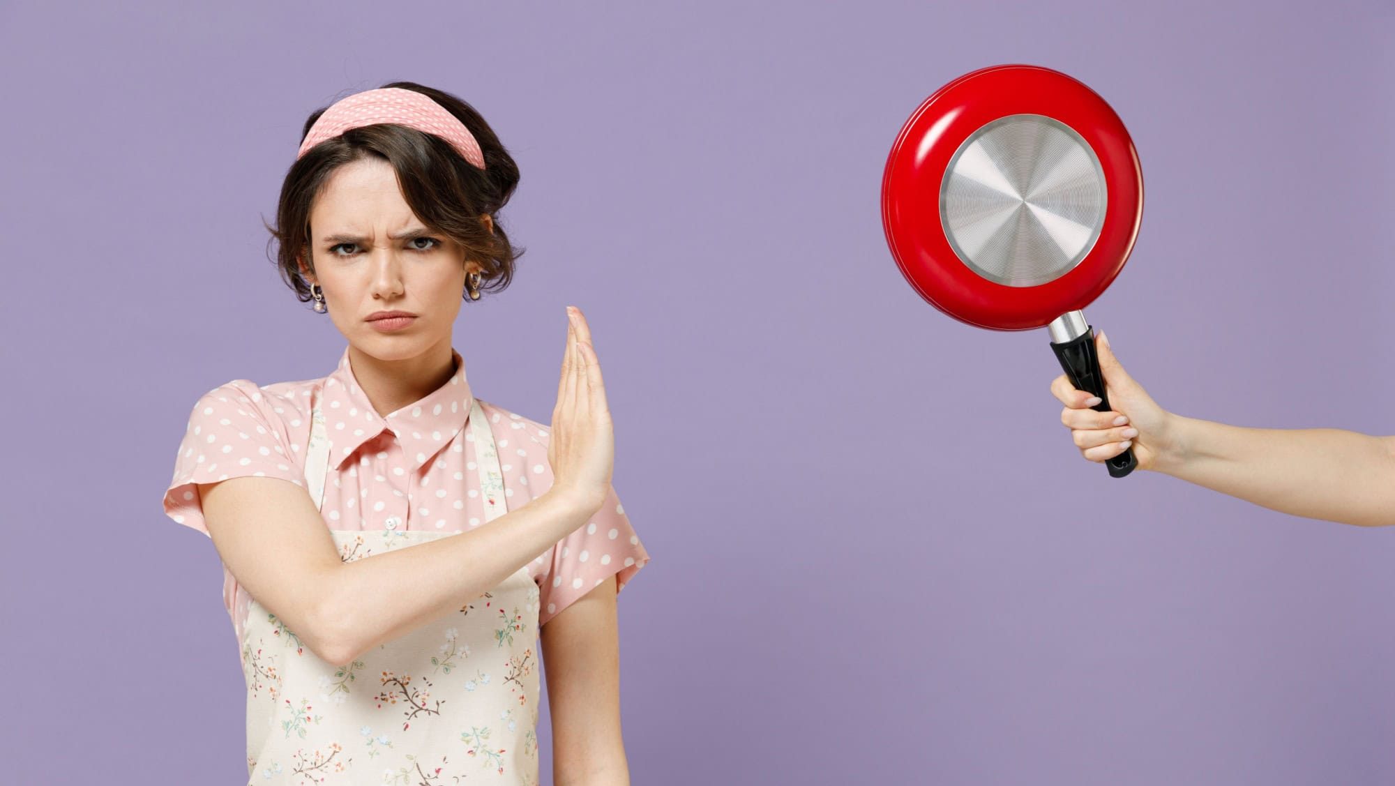 Young serious sad housewife housekeeper chef cook baker woman in pink apron hand hold red pan show stop palm gesture isolated on pastel violet background studio portrait Cooking food process concept.