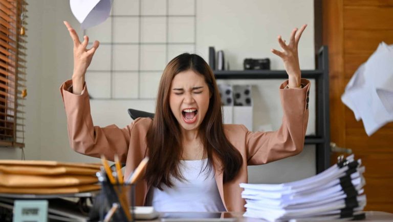 Angered, furious, crazy and mad millennial Asian businesswoman or female office worker screaming, shouting and throwing up papers at her office desk. Depression, overworked, failure.