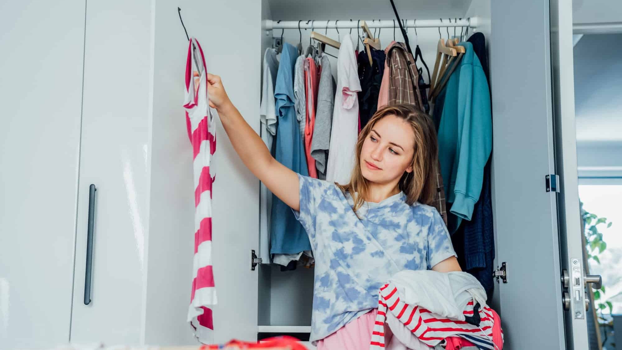 Woman selecting clothes from her wardrobe for donating to a Charity shop. Decluttering, Sorting clothes and Cleaning Up. Reuse, second-hand concept. Conscious consumer, sustainable lifestyle.