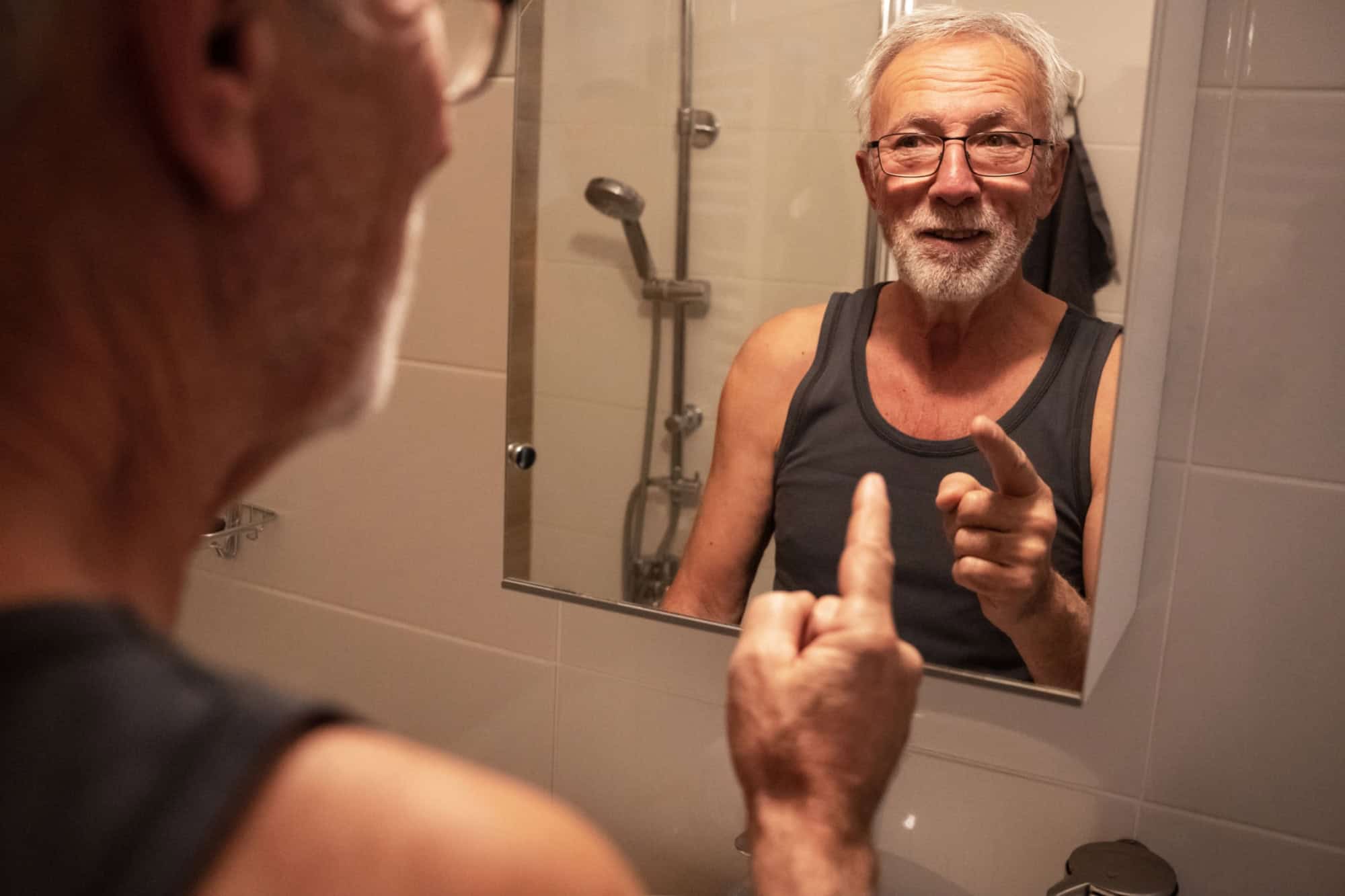 Confident senior man looking at his reflection in the mirror and talk to himself.