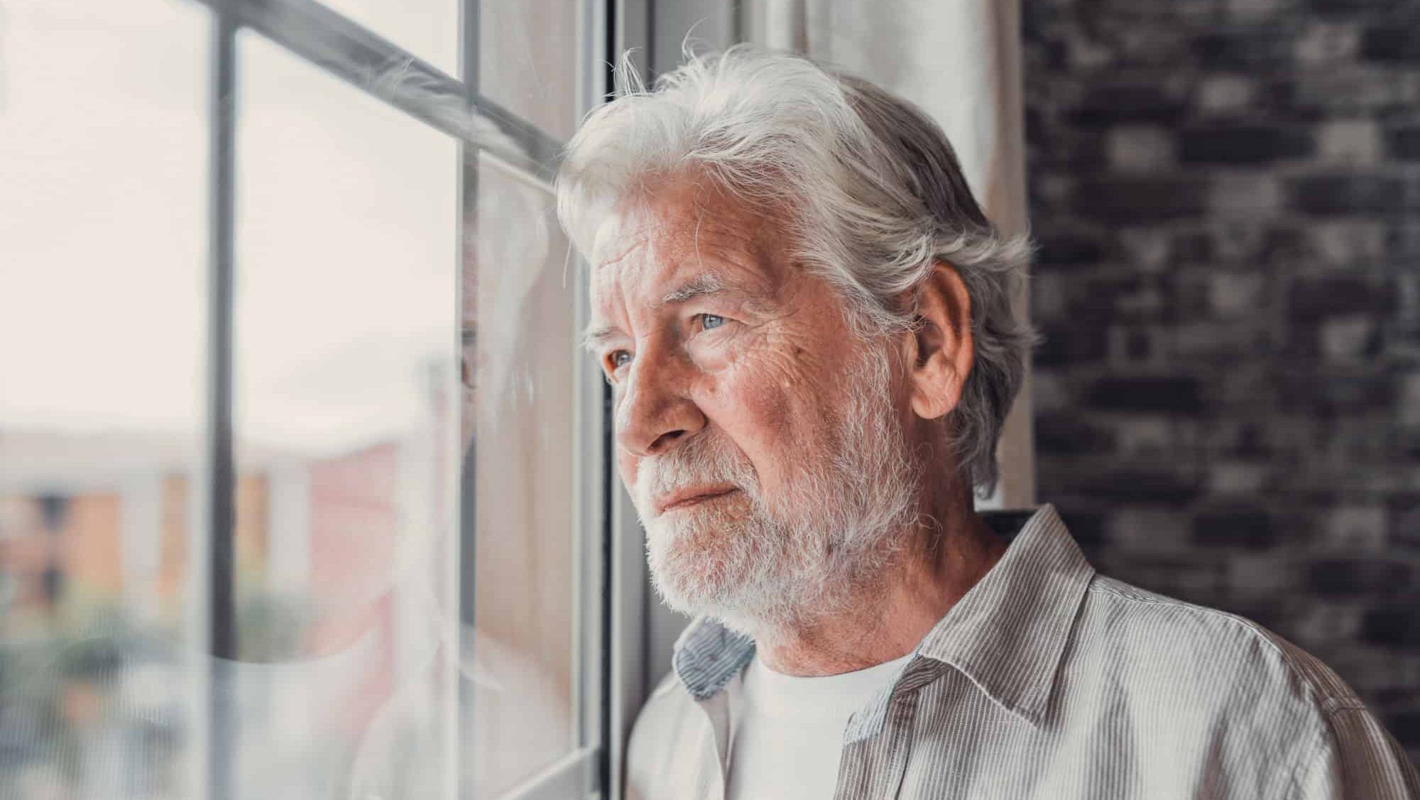 Pensive elderly mature senior man in eyeglasses looking in distance out of window, thinking of personal problems