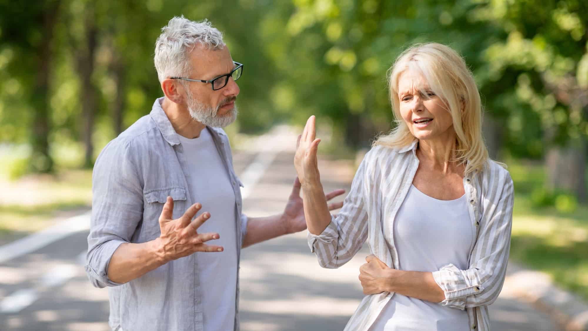 Older Couple Conflicts. Mature Spouses Arguing While Walking In Park, Angry Senior Man And Woman Quarreling Outdoors, Suffering Misunderstanding And Marital Crisis