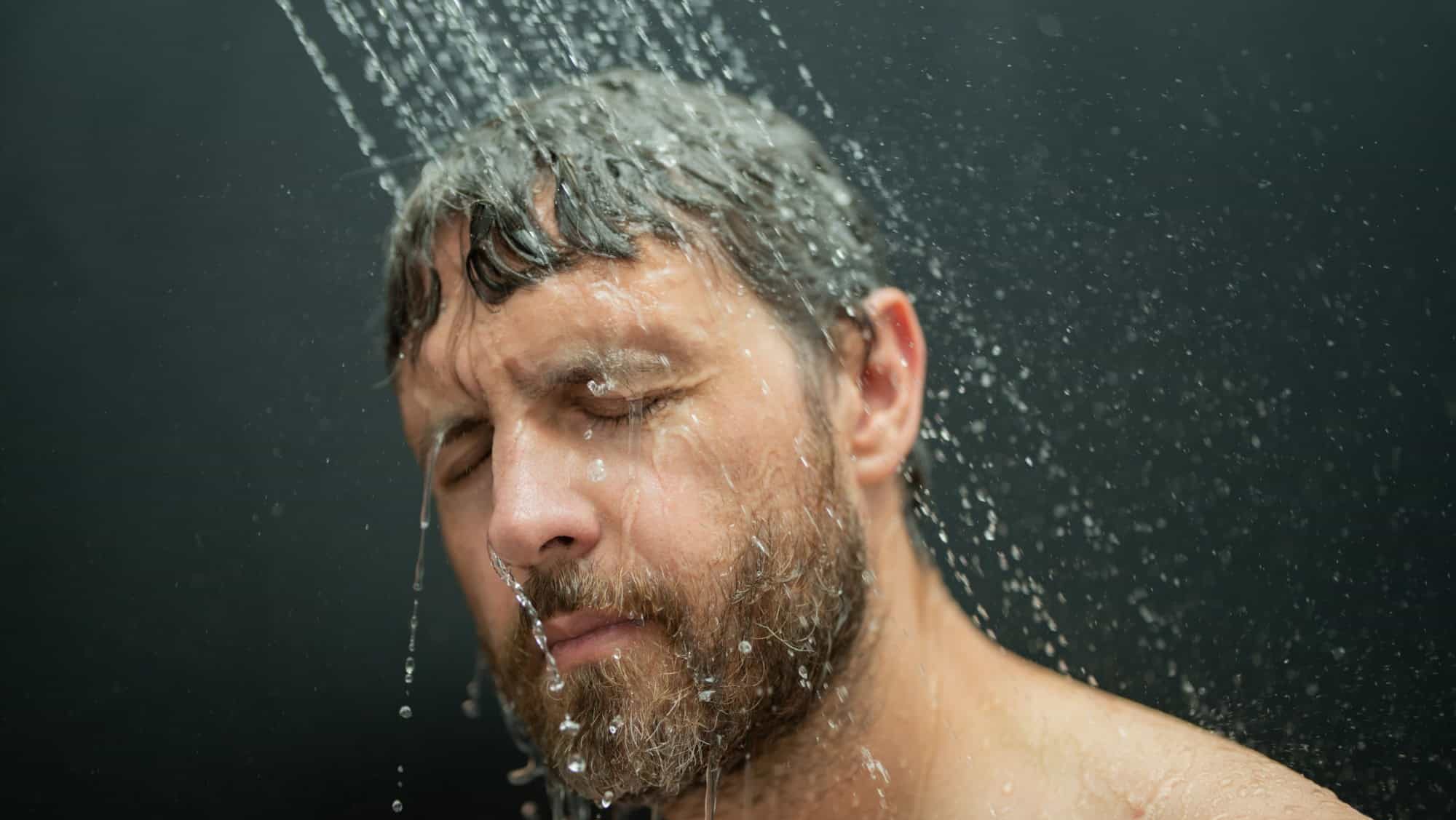 Man washing hair in bath. Guy bathing shower head in bathtub. Face in foam in shower. Bathing man taking shower. Close up guy showering. Shower concept. Man is under water drops in showers.