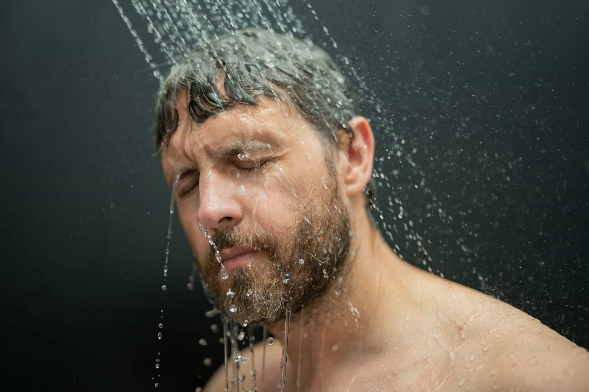 Man washing hair in bath. Guy bathing shower head in bathtub. Face in foam in shower. Bathing man taking shower. Close up guy showering. Shower concept. Man is under water drops in showers.