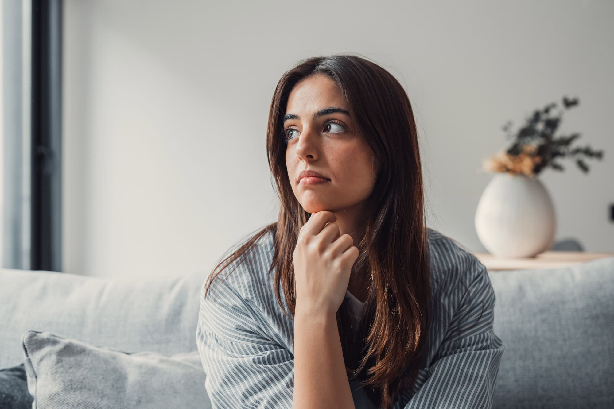 Close up of sad pensive millennial woman sit alone thinking about relationships personal problems, upset thoughtful young female lost in thoughts feel lonely depressed pondering or mourning at home