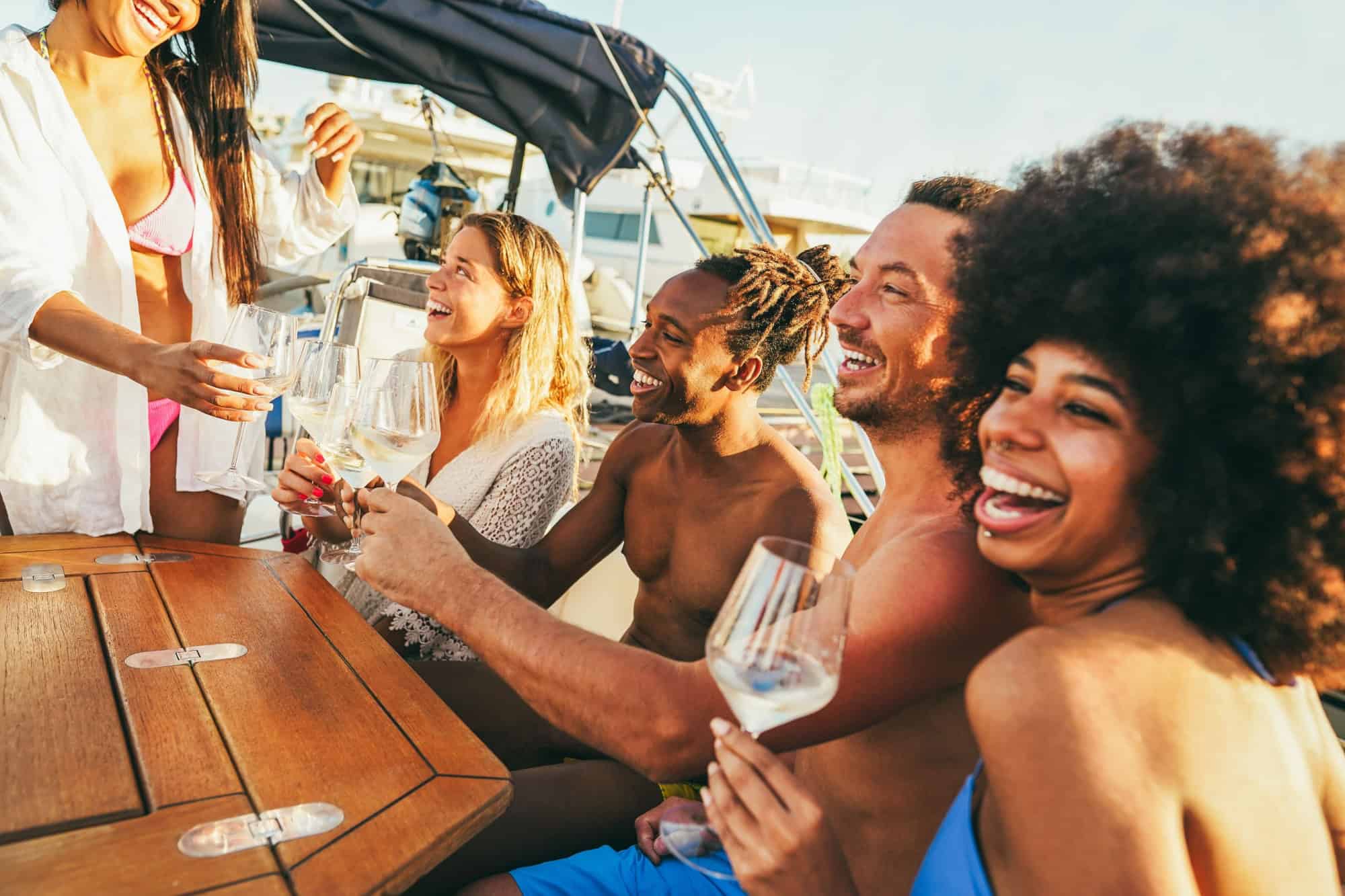 Multiracial friends having fun at boat party during summer vacation - Happy people cheering with champagne inside sailing cruis at sunset - Travel and holidays concept - Main focus on african man face
